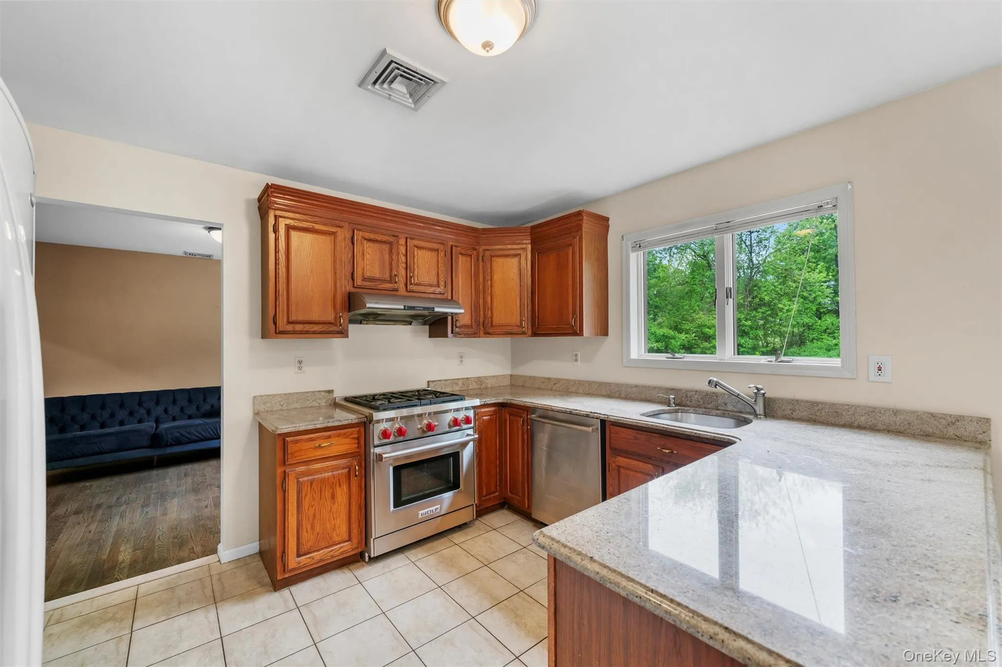 Kitchen featuring light stone countertops, appliances with stainless steel finishes, light tile patterned flooring, and brown cabinetry Kitchen featuring light stone countertops, appliances with stainless steel finishes, light tile patterned flooring, and brown cabinetry