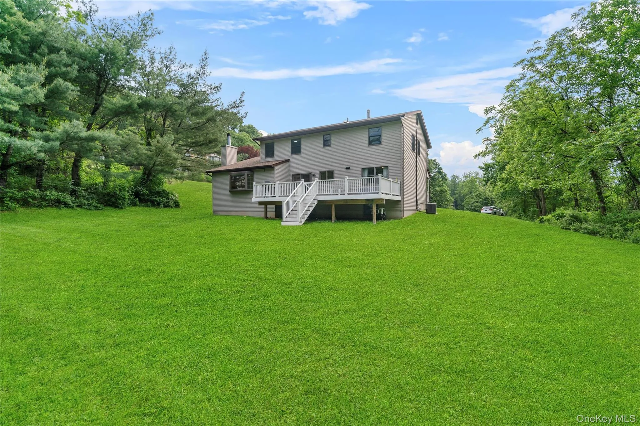 Back of house with a lawn, a deck, a chimney, and stairs Back of house with a lawn, a deck, a chimney, and stairs