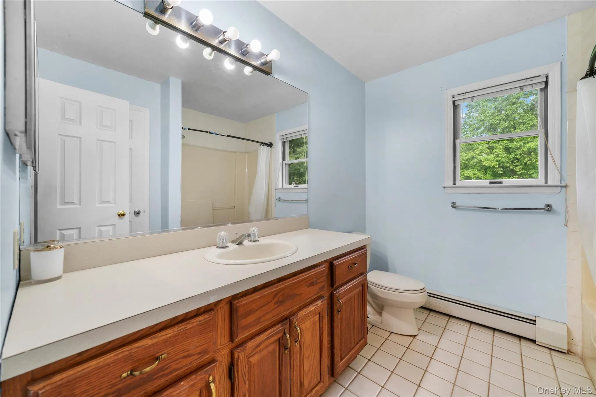 Bathroom featuring baseboard heating, vanity, curtained shower, and light tile patterned flooring Bathroom featuring baseboard heating, vanity, curtained shower, and light tile patterned flooring