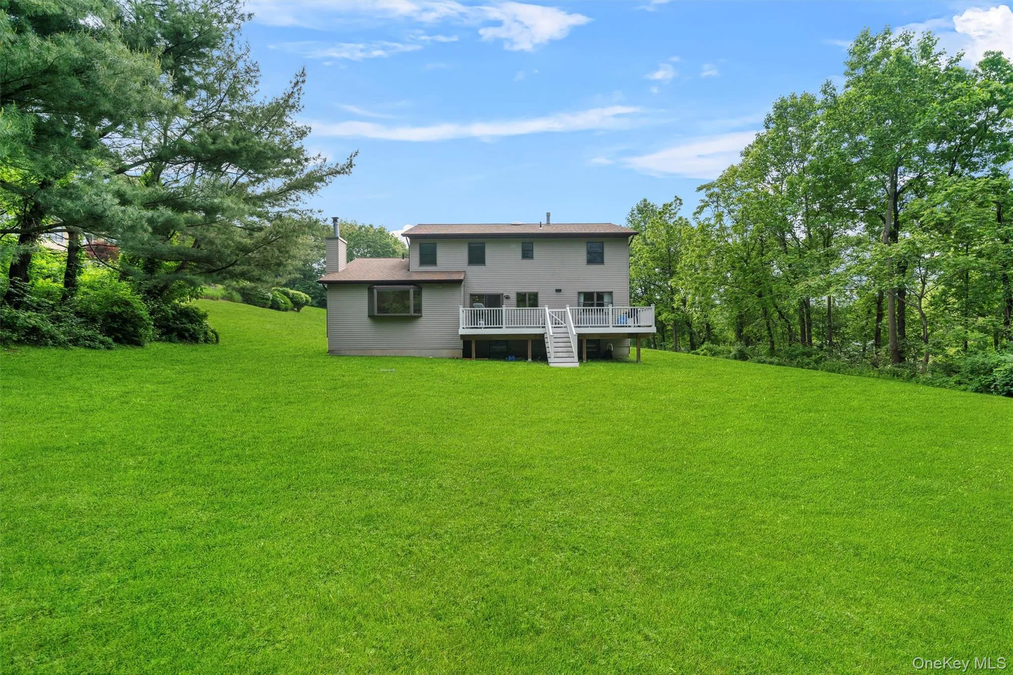 Rear view of property featuring a lawn, a deck, a chimney, and stairway Rear view of property featuring a lawn, a deck, a chimney, and stairway