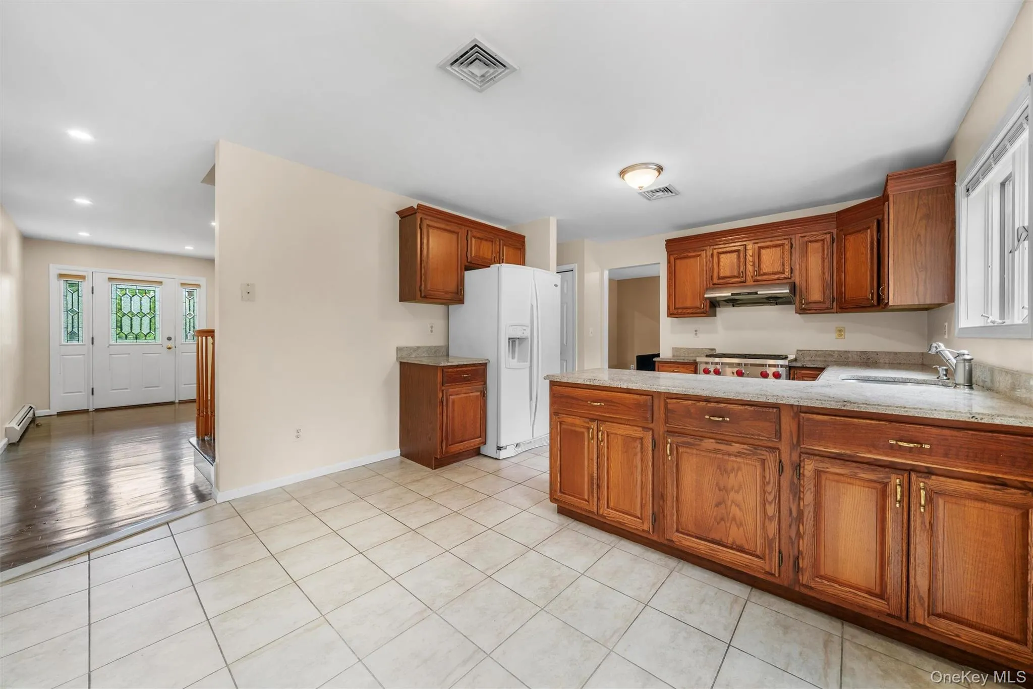 Kitchen with white refrigerator with ice dispenser, brown cabinetry, light tile patterned floors, and a peninsula Kitchen with white refrigerator with ice dispenser, brown cabinetry, light tile patterned floors, and a peninsula