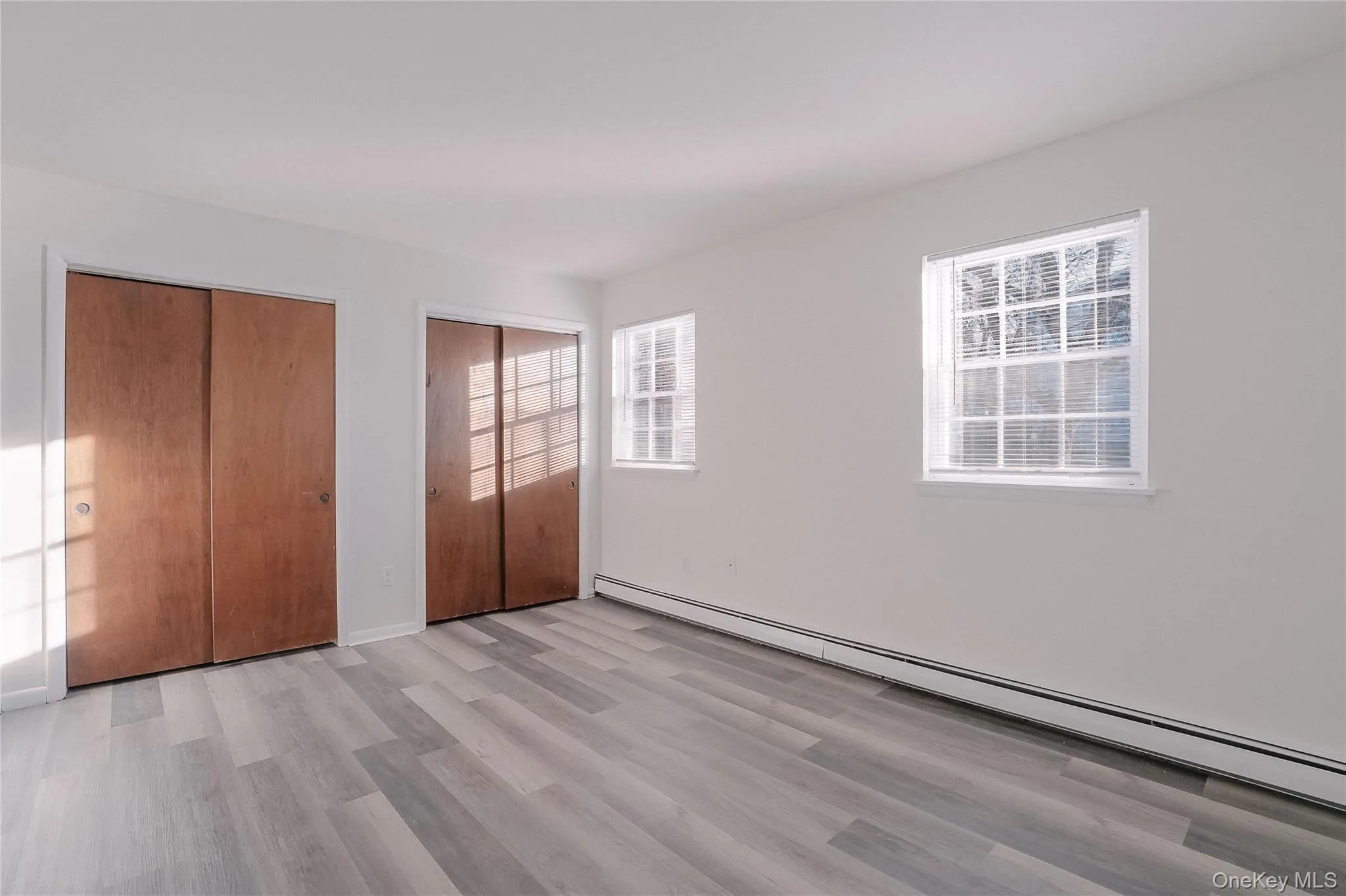 Unfurnished bedroom featuring a baseboard heating unit, multiple closets, and light wood-style flooring Unfurnished bedroom featuring a baseboard heating unit, multiple closets, and light wood-style flooring