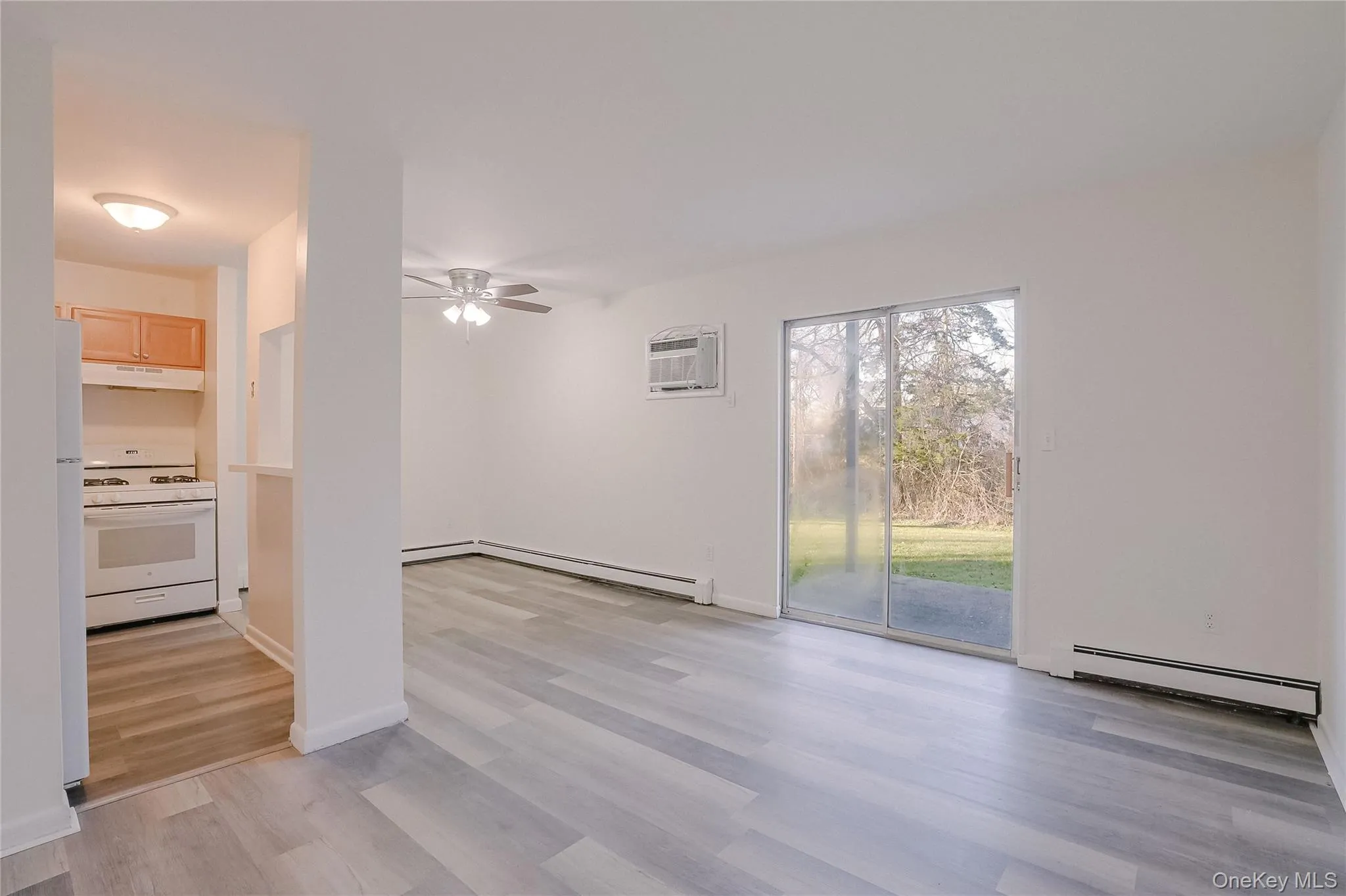 Unfurnished living room with a ceiling fan, a baseboard radiator, light wood-style flooring, and a wall unit AC Unfurnished living room with a ceiling fan, a baseboard radiator, light wood-style flooring, and a wall unit AC