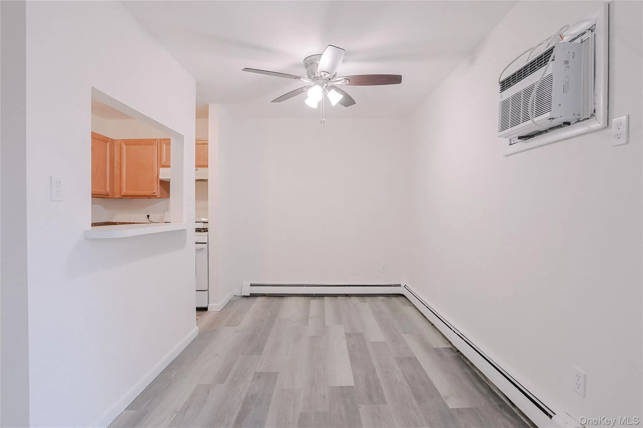 Empty room featuring a baseboard heating unit, light wood finished floors, an AC wall unit, and ceiling fan Empty room featuring a baseboard heating unit, light wood finished floors, an AC wall unit, and ceiling fan