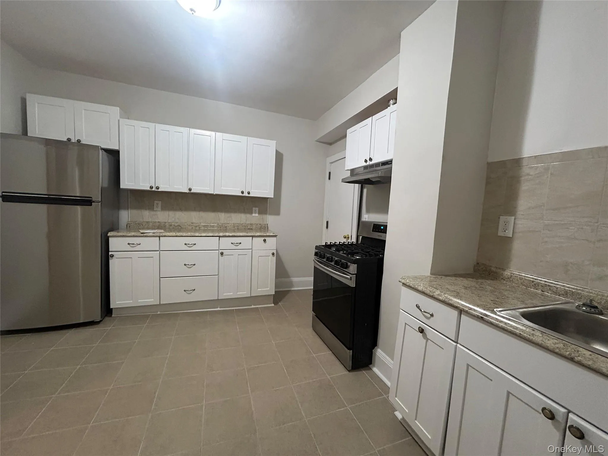 Kitchen with stainless steel appliances, white cabinetry, under cabinet range hood, decorative backsplash, and light tile patterned floors Kitchen with stainless steel appliances, white cabinetry, under cabinet range hood, decorative backsplash, and light tile patterned floors
