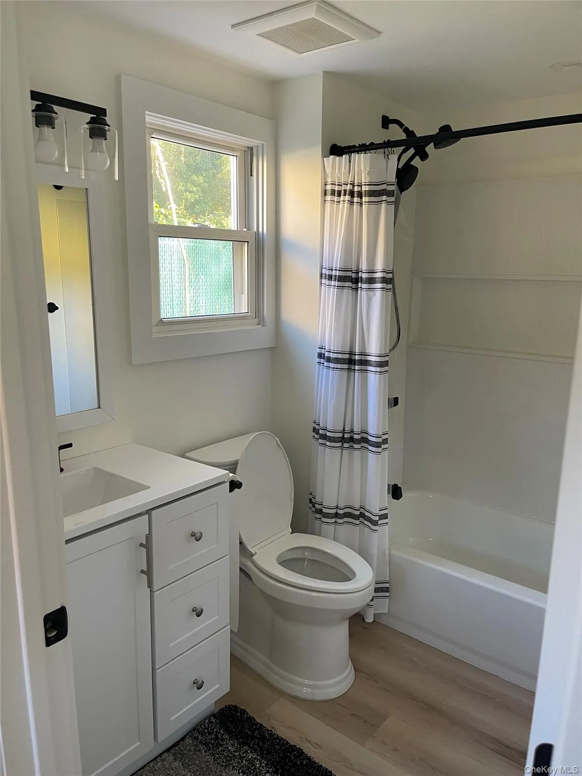 Full bathroom with vanity, shower / tub combo, and light wood finished floors Full bathroom with vanity, shower / tub combo, and light wood finished floors