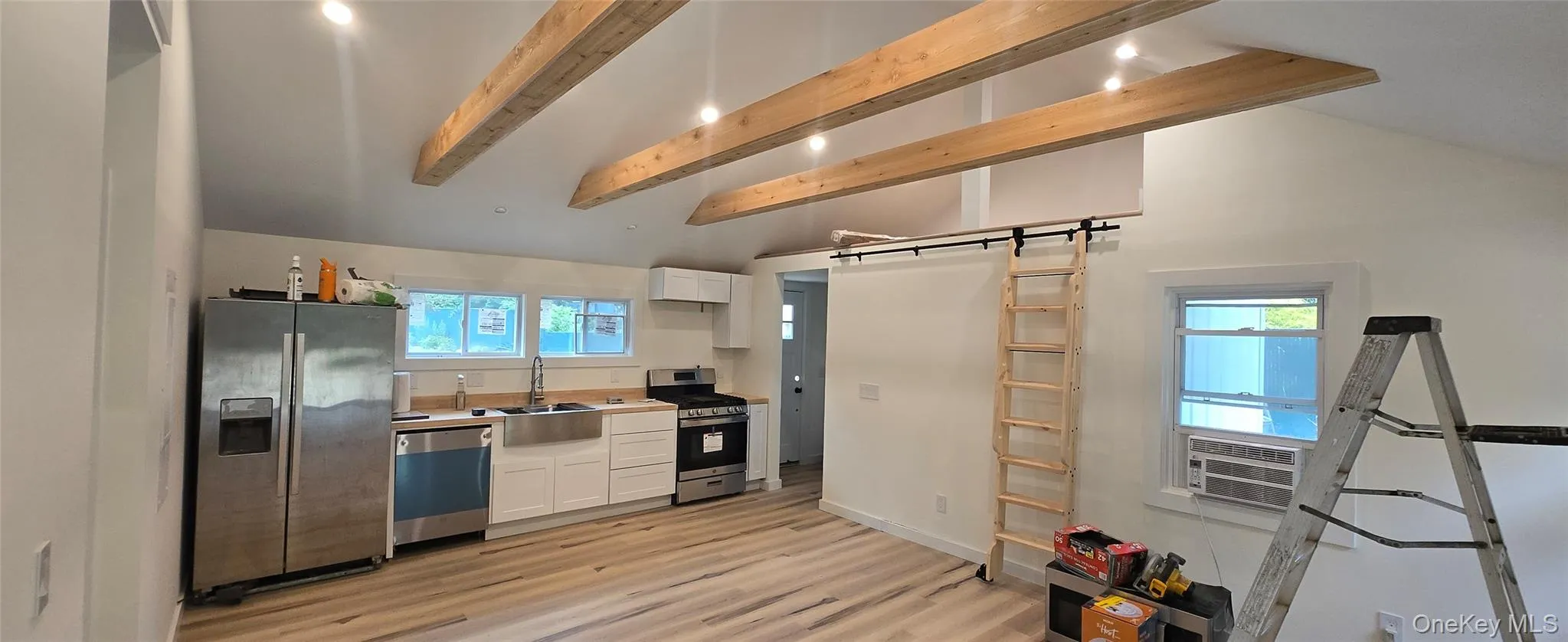 Kitchen with white cabinets, stainless steel appliances, light countertops, beamed ceiling, and light wood finished floors Kitchen with white cabinets, stainless steel appliances, light countertops, beamed ceiling, and light wood finished floors