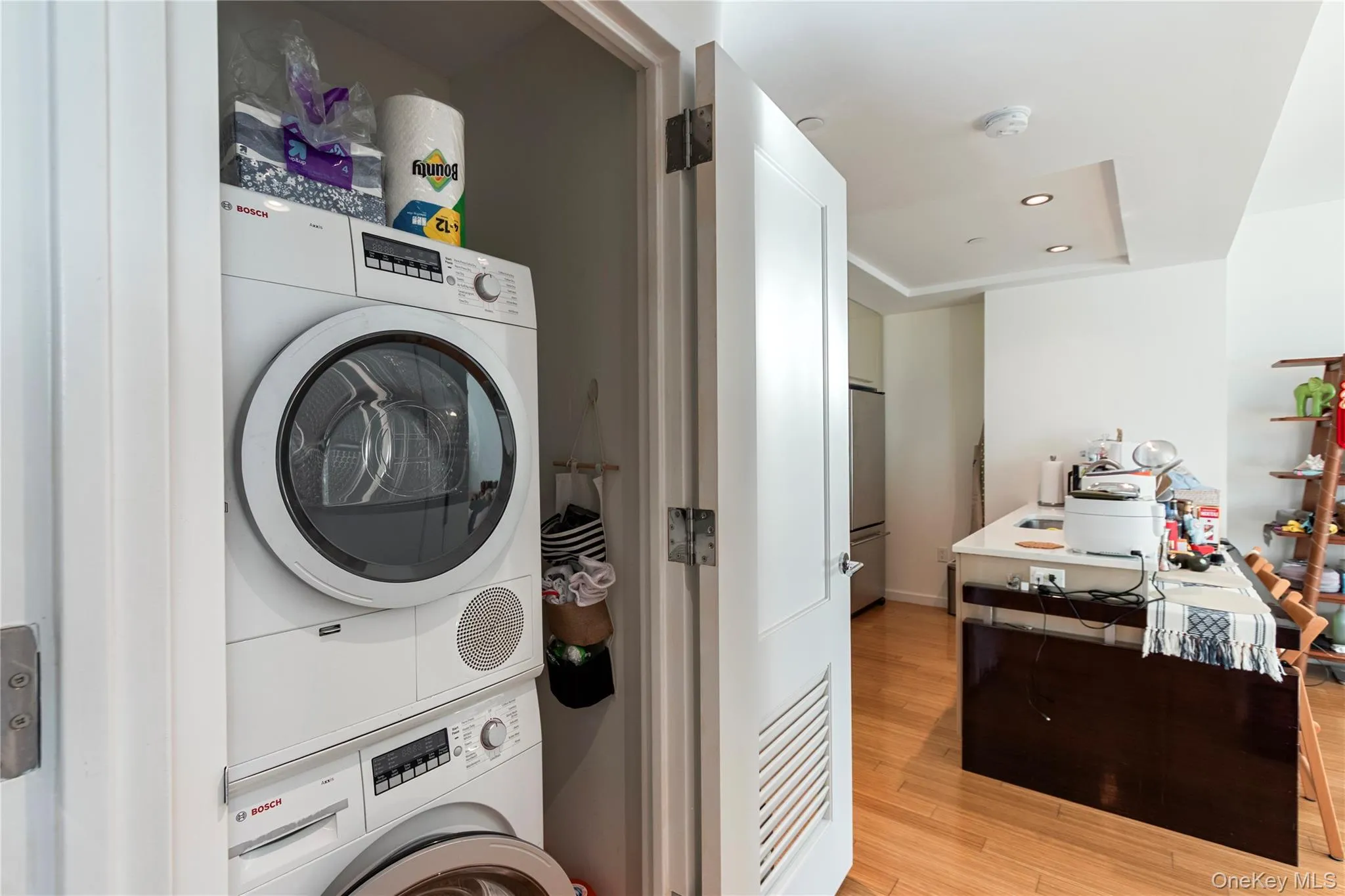 Laundry room featuring stacked washing machine and dryer, light wood finished floors, and recessed lighting Laundry room featuring stacked washing machine and dryer, light wood finished floors, and recessed lighting