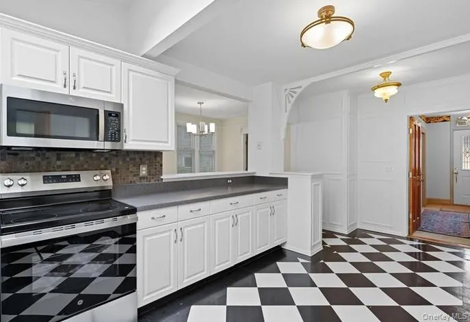 Kitchen with appliances with stainless steel finishes, white cabinets, dark countertops, and decorative backsplash Kitchen with appliances with stainless steel finishes, white cabinets, dark countertops, and decorative backsplash