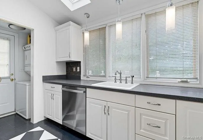 Kitchen featuring dark countertops, white cabinetry, dishwasher, a skylight, and pendant lighting Kitchen featuring dark countertops, white cabinetry, dishwasher, a skylight, and pendant lighting