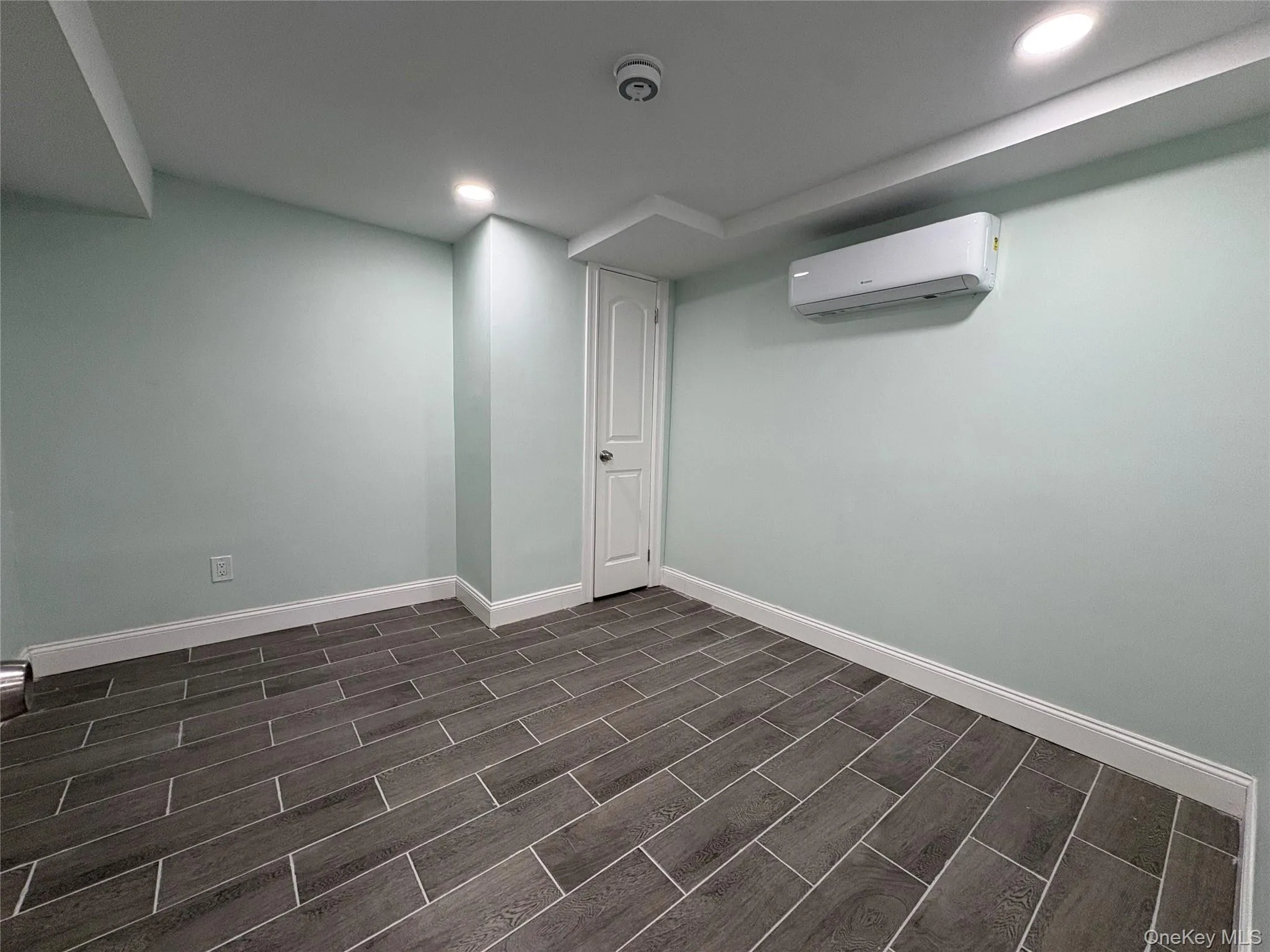 Below grade area with a wall mounted AC, recessed lighting, and wood finish floors Below grade area with a wall mounted AC, recessed lighting, and wood finish floors