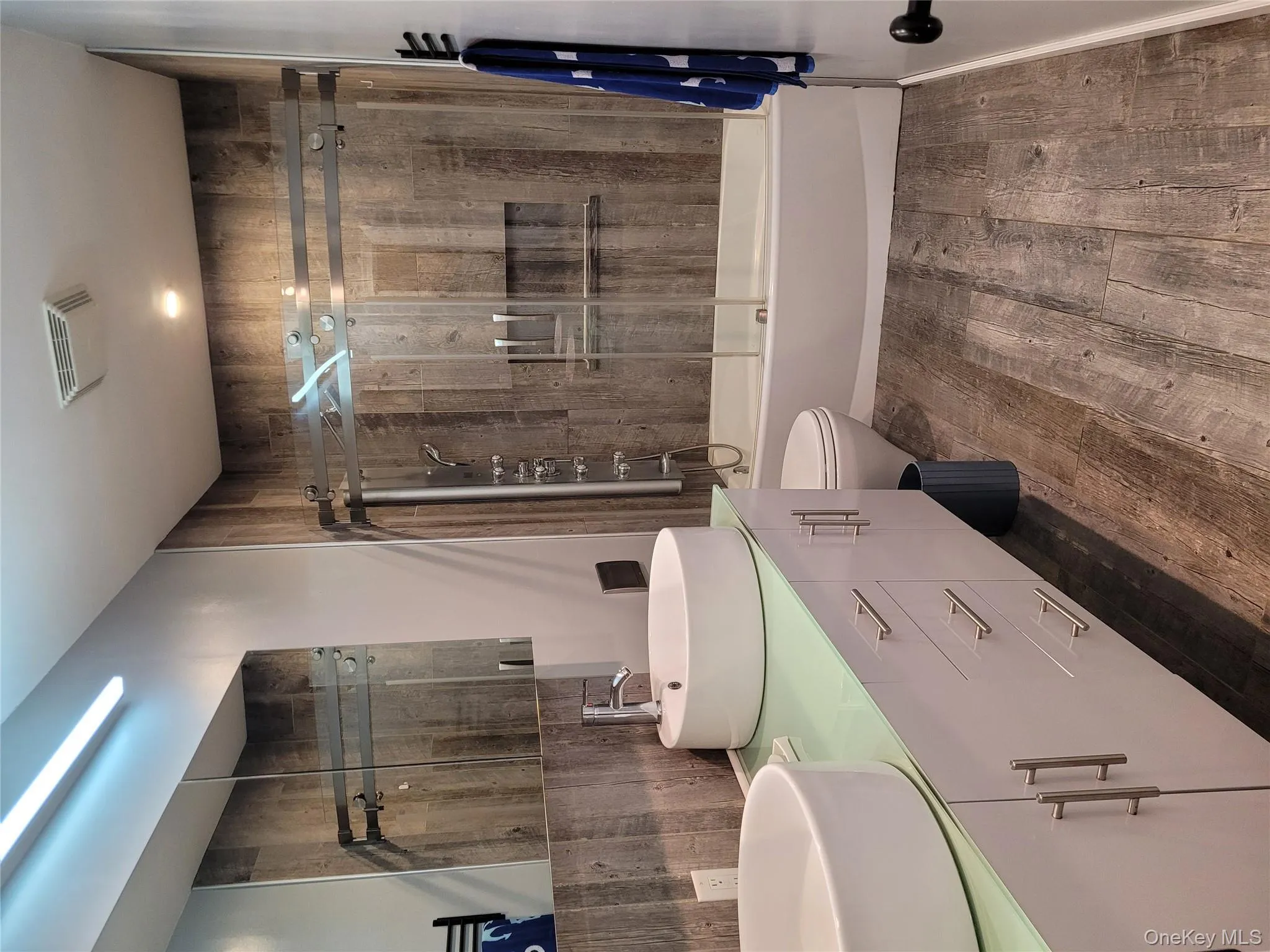 Full bath featuring wood finished floors, shower / bath combination with glass door, and double vanity Full bath featuring wood finished floors, shower / bath combination with glass door, and double vanity