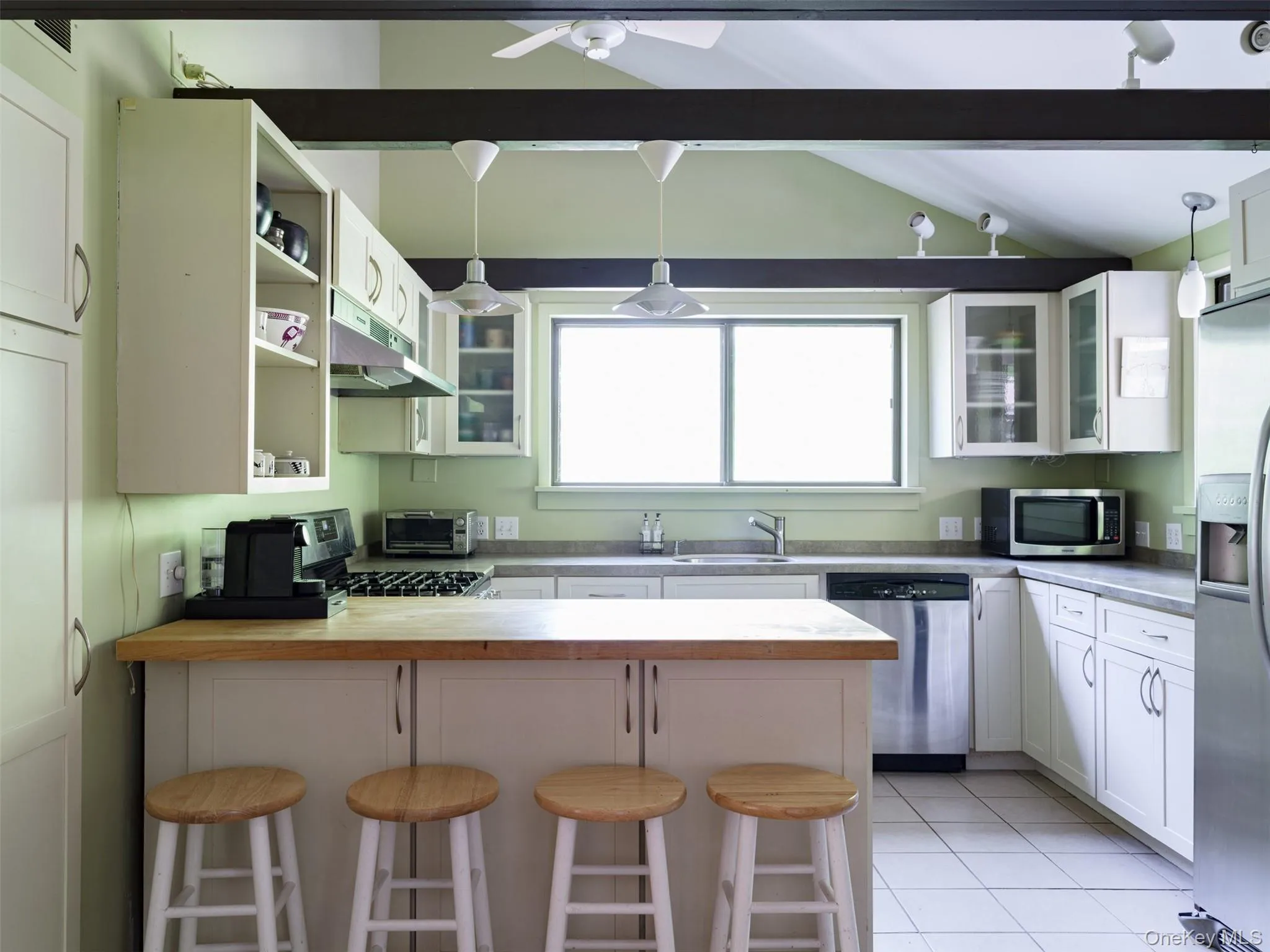 Kitchen featuring a peninsula, a breakfast bar area, glass insert cabinets, wooden counters, and stainless steel appliances Kitchen featuring a peninsula, a breakfast bar area, glass insert cabinets, wooden counters, and stainless steel appliances