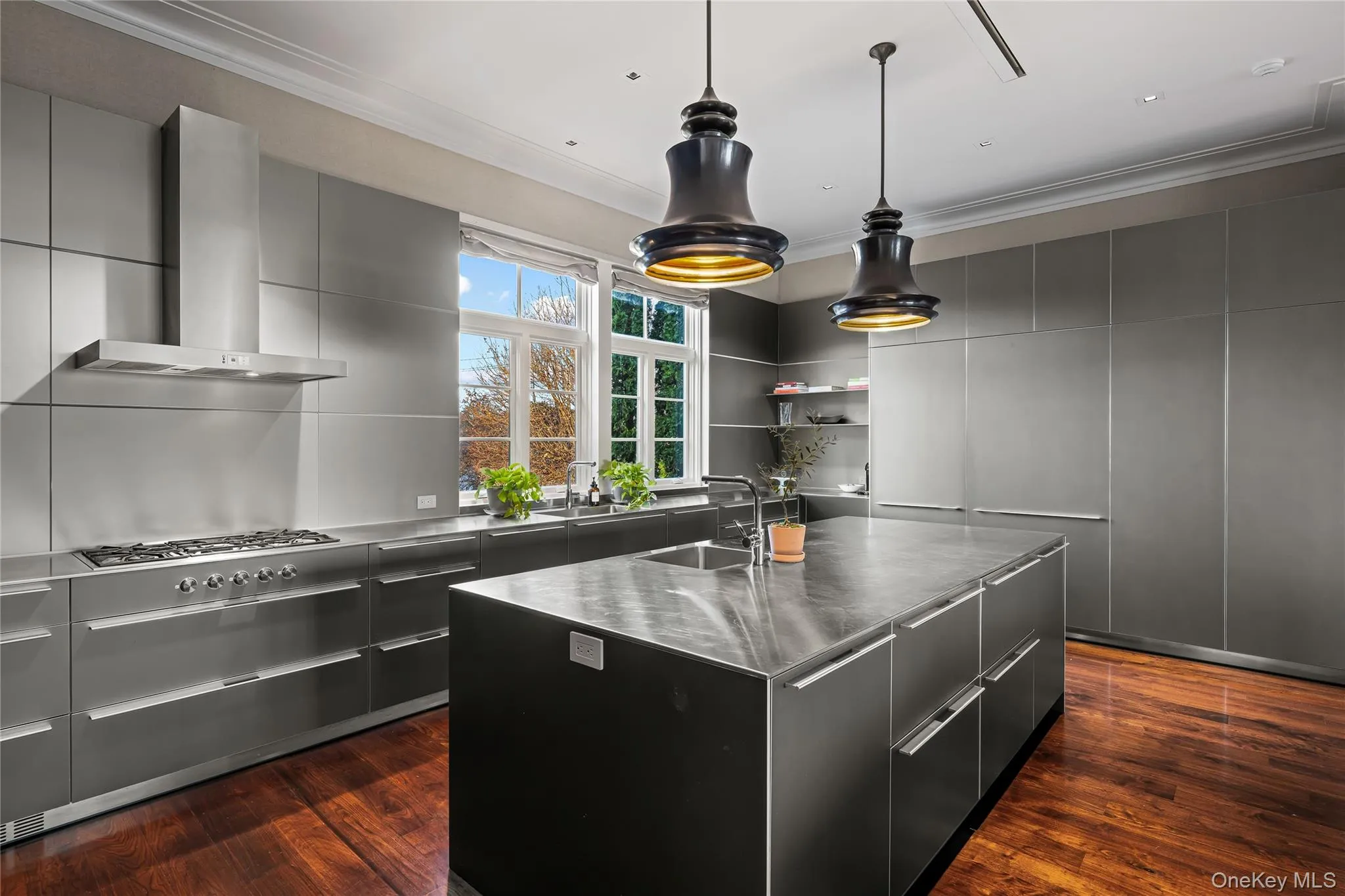 Kitchen with modern cabinets, stainless steel counters, ornamental molding, wall chimney range hood, and a center island Kitchen with modern cabinets, stainless steel counters, ornamental molding, wall chimney range hood, and a center island