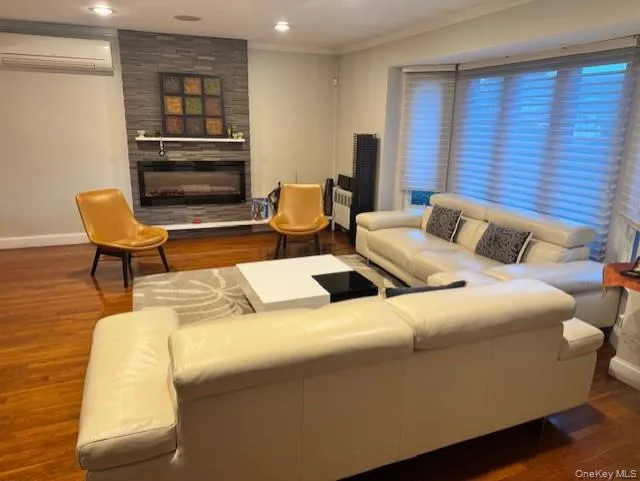 Living room featuring dark wood-style floors, a fireplace, radiator heating unit, a wall mounted air conditioner, and recessed lighting Living room featuring dark wood-style floors, a fireplace, radiator heating unit, a wall mounted air conditioner, and recessed lighting