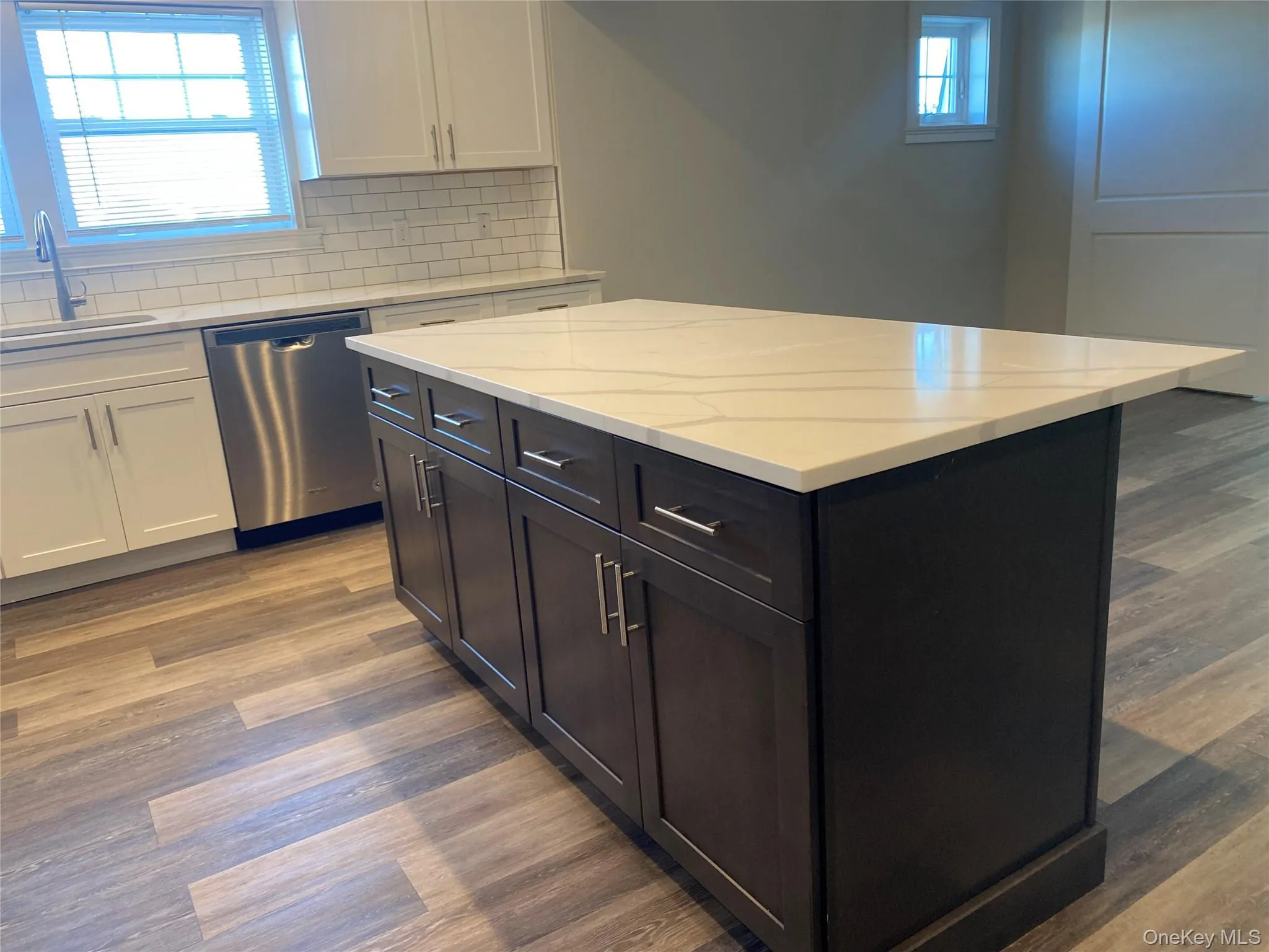 Kitchen with white cabinetry, a kitchen island, dark wood-style flooring, and stainless steel dishwasher Kitchen with white cabinetry, a kitchen island, dark wood-style flooring, and stainless steel dishwasher