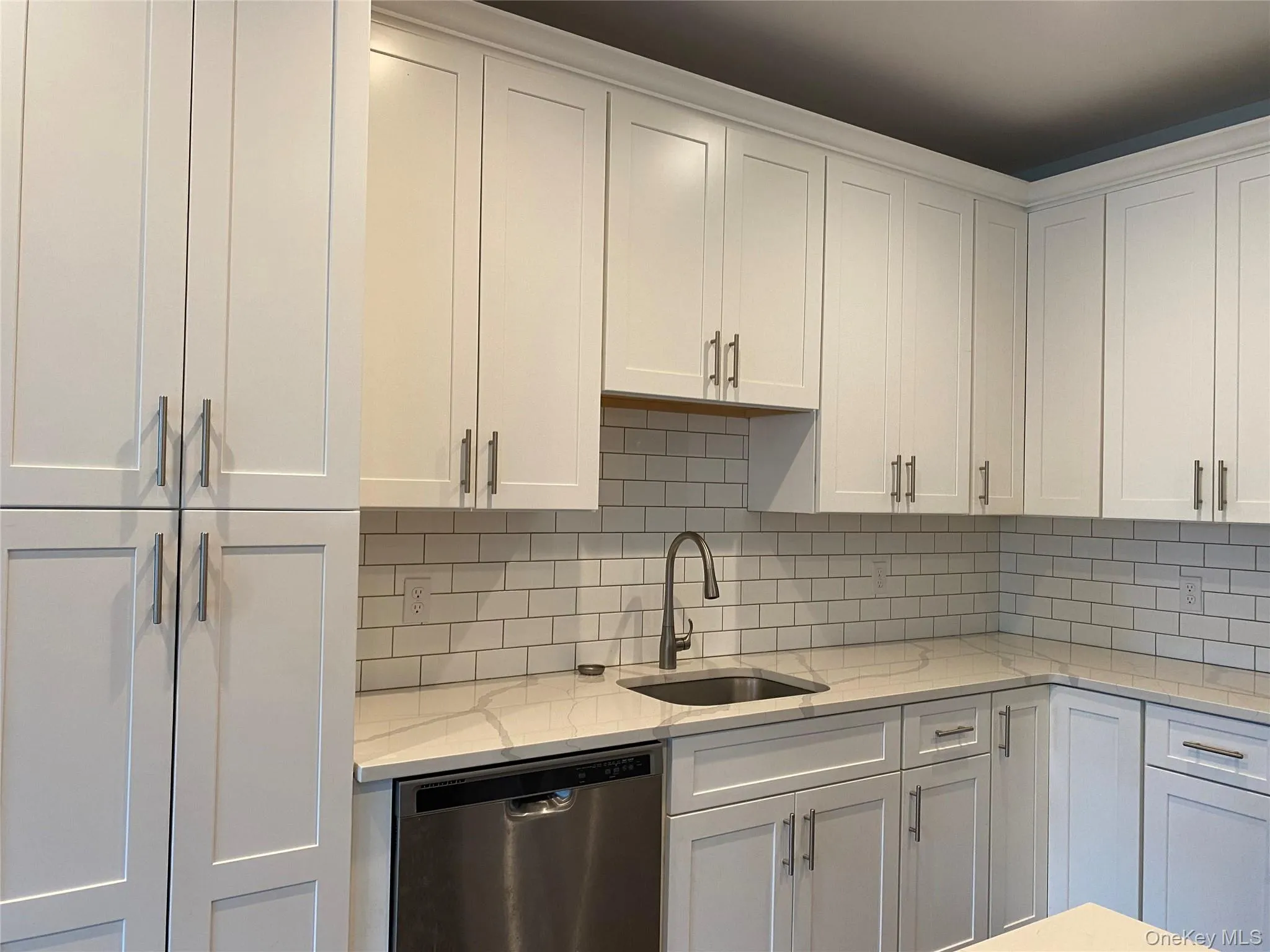 Kitchen featuring light stone counters, dishwasher, and white cabinets Kitchen featuring light stone counters, dishwasher, and white cabinets