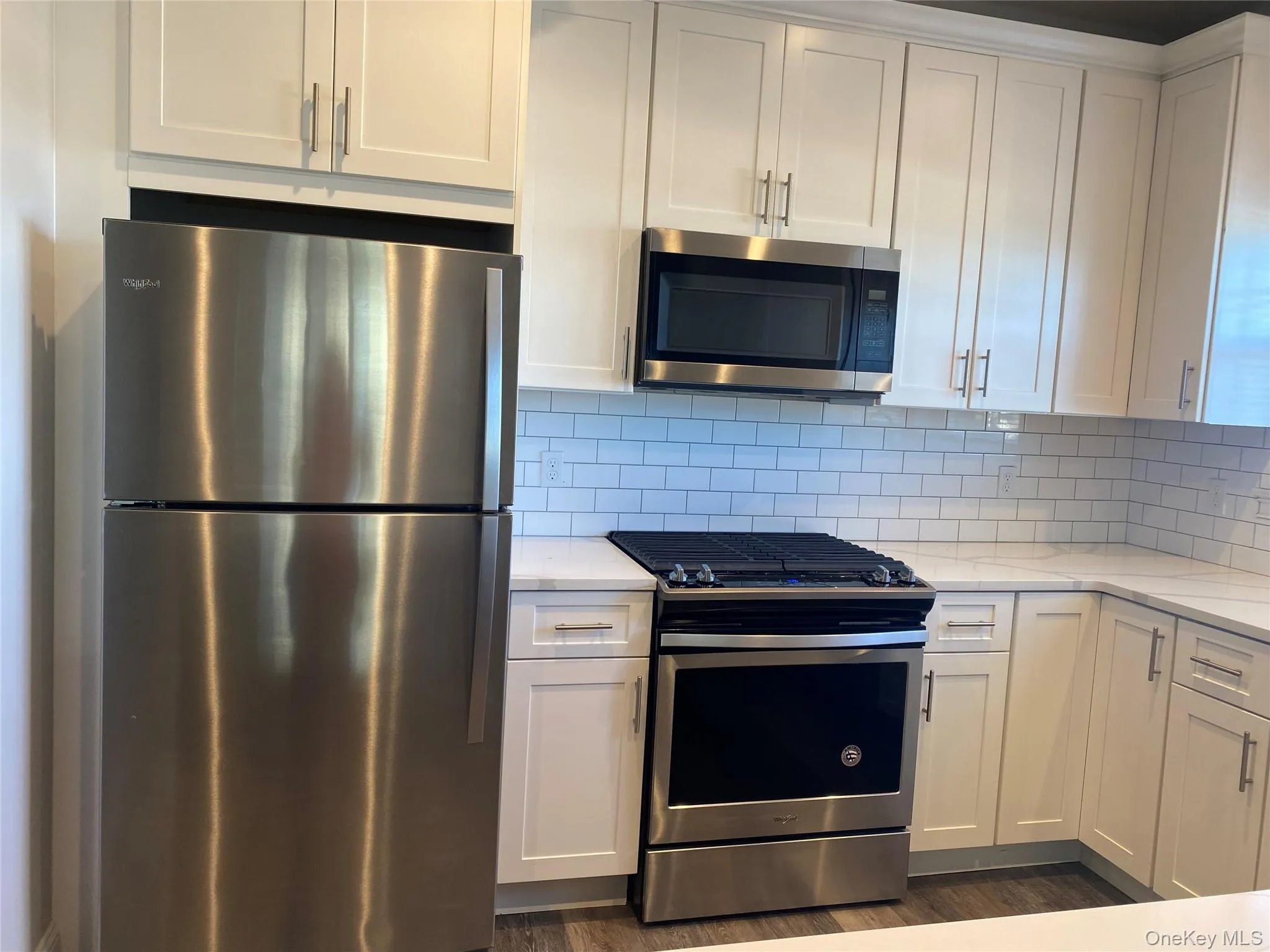 Kitchen featuring appliances with stainless steel finishes, white cabinetry, light stone countertops, tasteful backsplash, and dark wood-type flooring Kitchen featuring appliances with stainless steel finishes, white cabinetry, light stone countertops, tasteful backsplash, and dark wood-type flooring