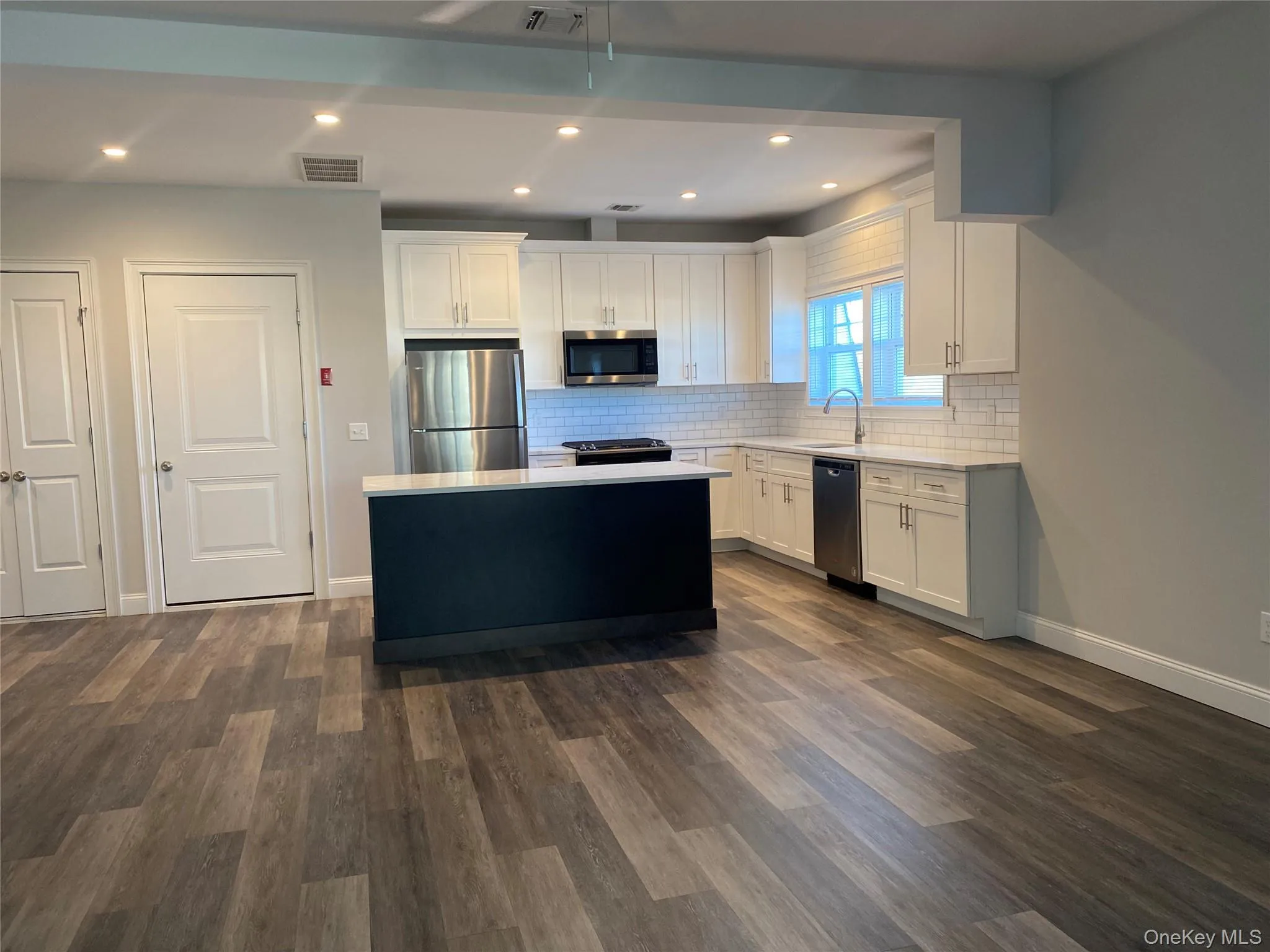 Kitchen with white cabinetry, a kitchen island, stainless steel appliances, recessed lighting, and dark wood-type flooring Kitchen with white cabinetry, a kitchen island, stainless steel appliances, recessed lighting, and dark wood-type flooring