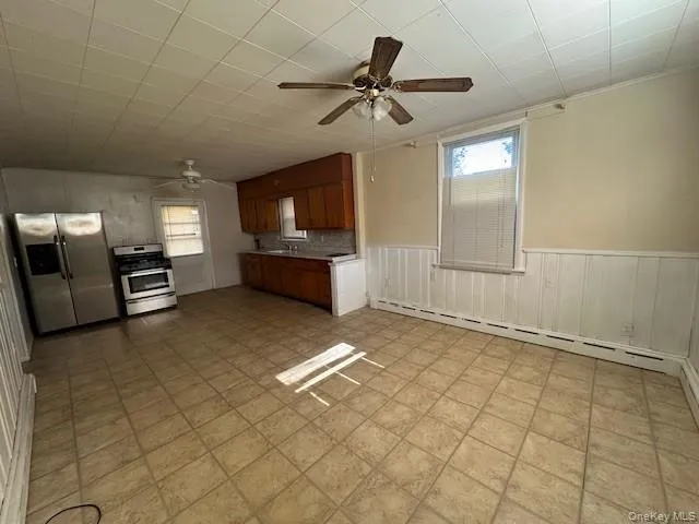 Kitchen featuring brown cabinetry, a ceiling fan, appliances with stainless steel finishes, light countertops, and a baseboard radiator Kitchen featuring brown cabinetry, a ceiling fan, appliances with stainless steel finishes, light countertops, and a baseboard radiator