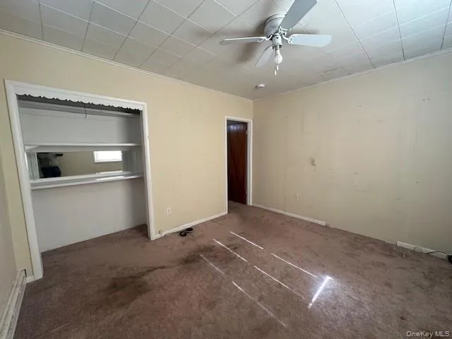 Unfurnished bedroom featuring carpet floors, a closet, a ceiling fan, and ornamental molding Unfurnished bedroom featuring carpet floors, a closet, a ceiling fan, and ornamental molding