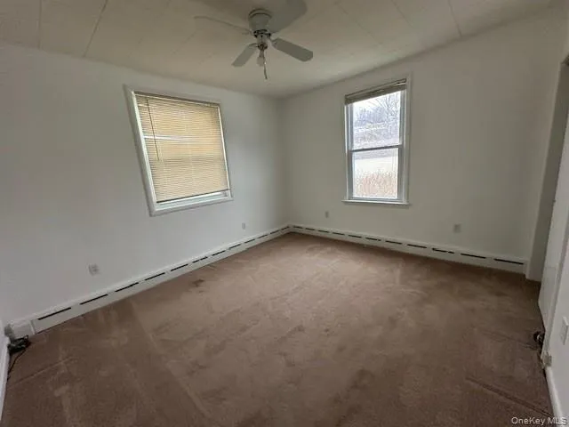 Carpeted empty room with baseboard heating, ceiling fan, and a baseboard heating unit Carpeted empty room with baseboard heating, ceiling fan, and a baseboard heating unit