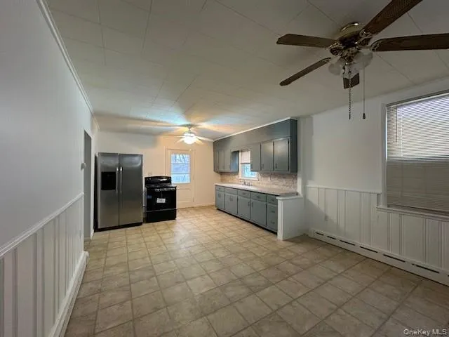 Kitchen featuring wainscoting, ceiling fan, stainless steel fridge, black range with electric cooktop, and light countertops Kitchen featuring wainscoting, ceiling fan, stainless steel fridge, black range with electric cooktop, and light countertops