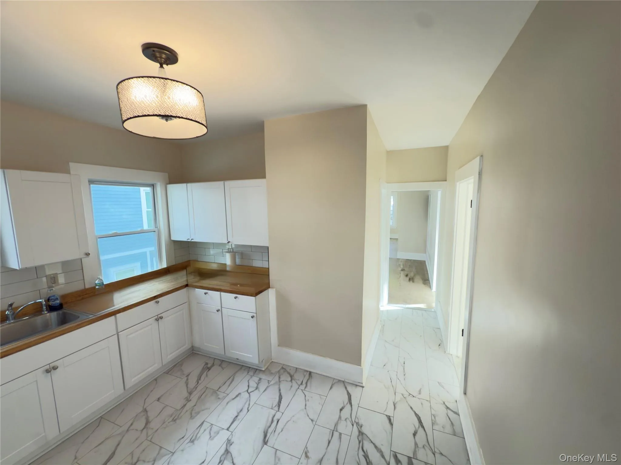 Kitchen featuring tasteful backsplash, light marble finish flooring, hanging light fixtures, and white cabinetry Kitchen featuring tasteful backsplash, light marble finish flooring, hanging light fixtures, and white cabinetry