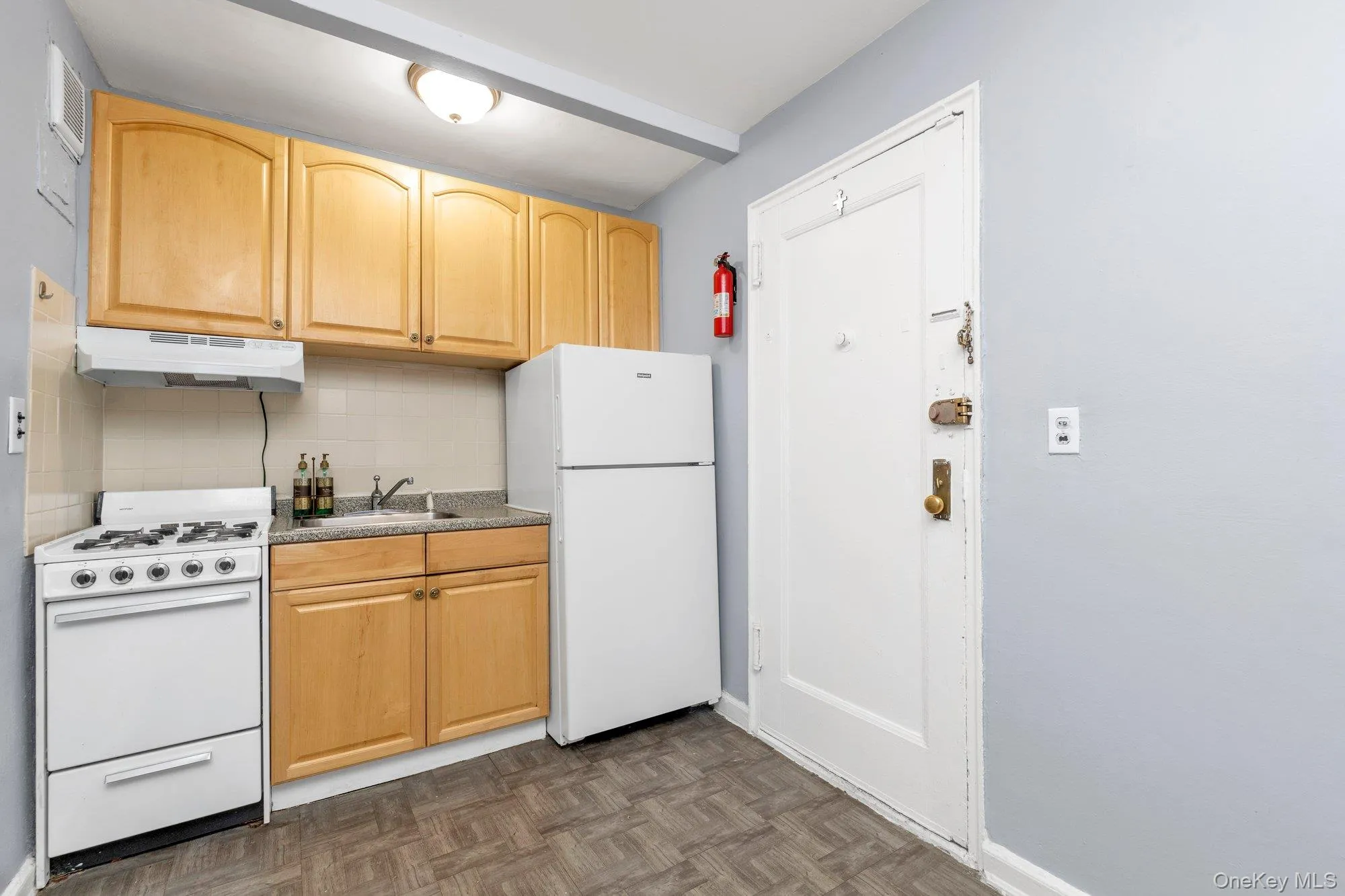 Kitchen with white appliances, backsplash, under cabinet range hood, light brown cabinets, and light countertops Kitchen with white appliances, backsplash, under cabinet range hood, light brown cabinets, and light countertops
