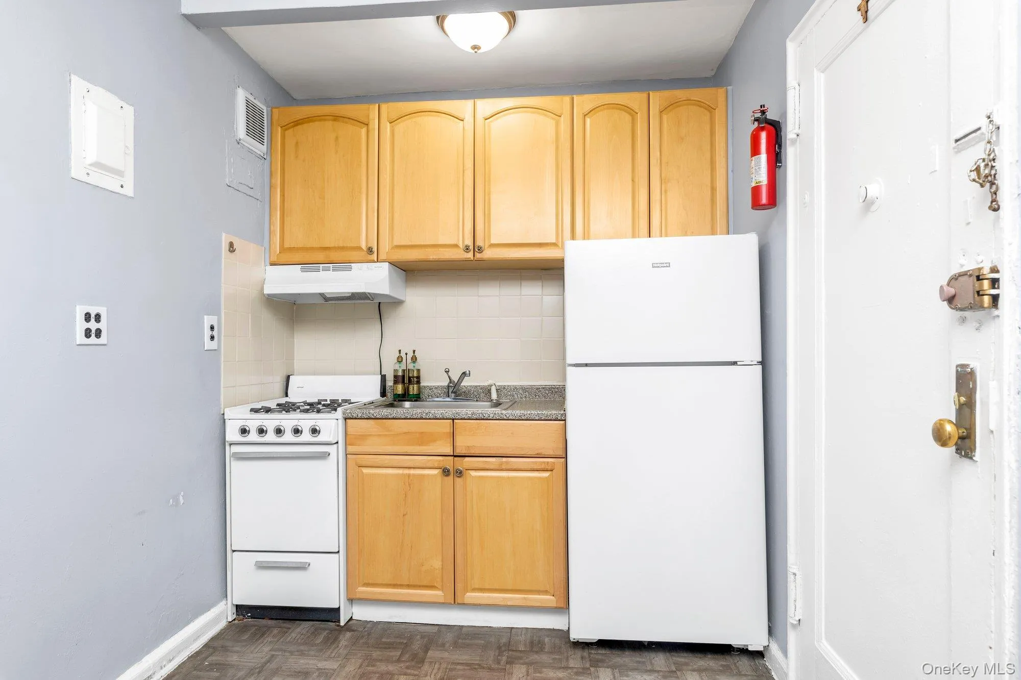 Kitchen featuring white appliances, tasteful backsplash, under cabinet range hood, light brown cabinets, and light countertops Kitchen featuring white appliances, tasteful backsplash, under cabinet range hood, light brown cabinets, and light countertops