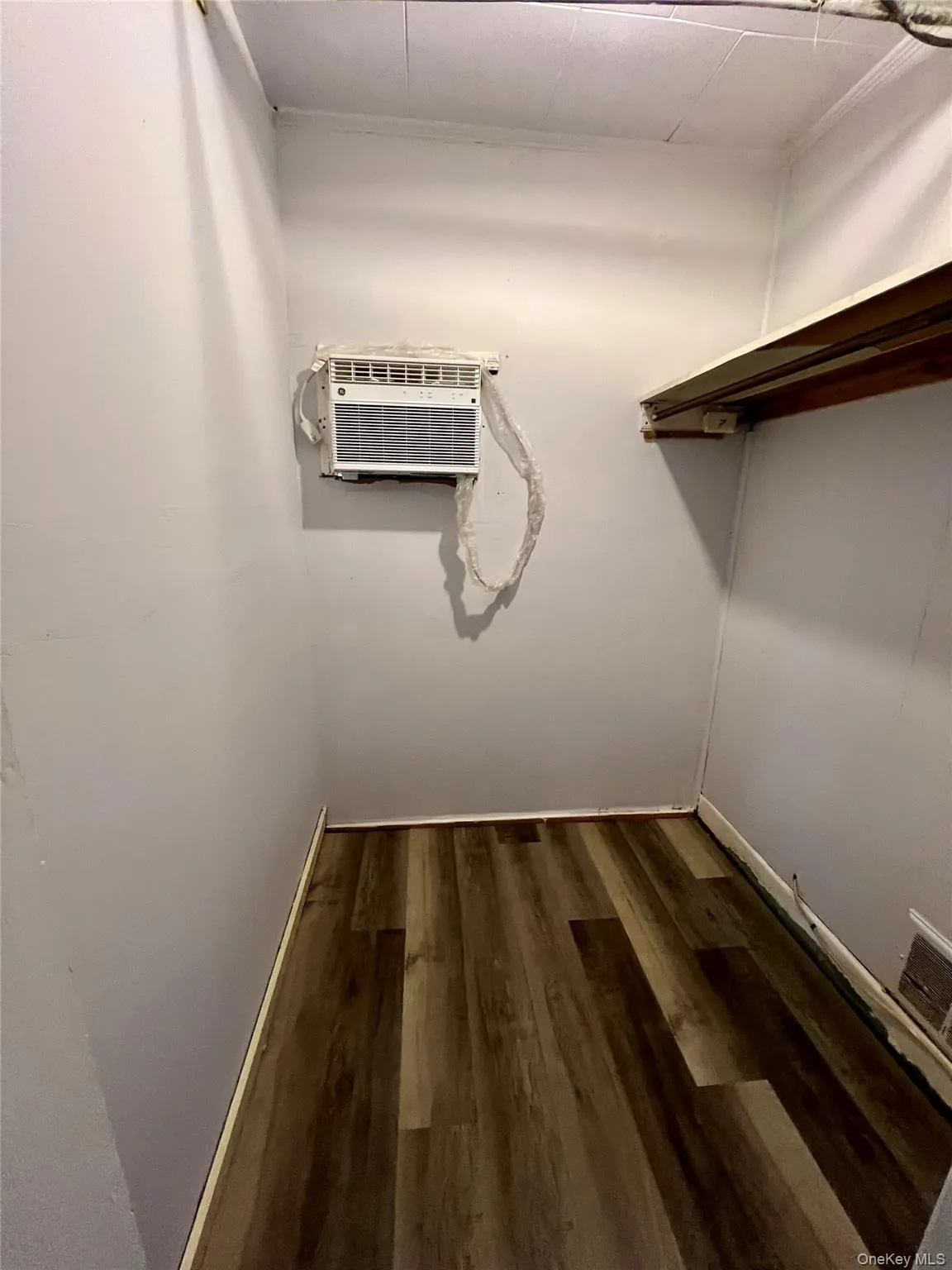 Walk in closet with dark wood-style flooring and an AC wall unit Walk in closet with dark wood-style flooring and an AC wall unit