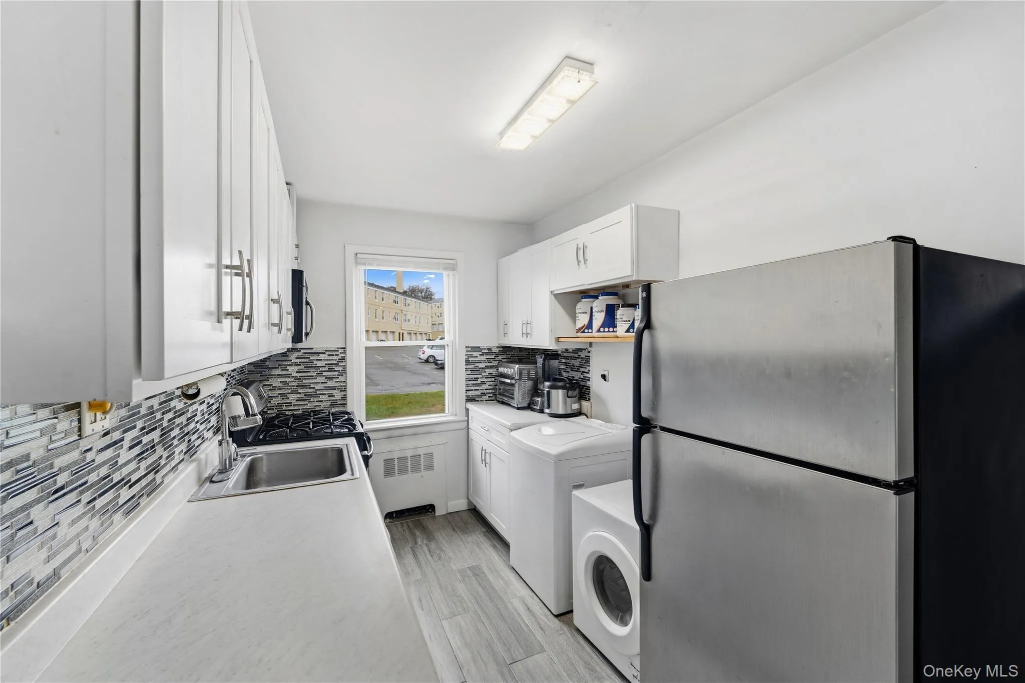 Kitchen featuring appliances with stainless steel finishes, white cabinetry, light countertops, decorative backsplash, and washer / clothes dryer Kitchen featuring appliances with stainless steel finishes, white cabinetry, light countertops, decorative backsplash, and washer / clothes dryer