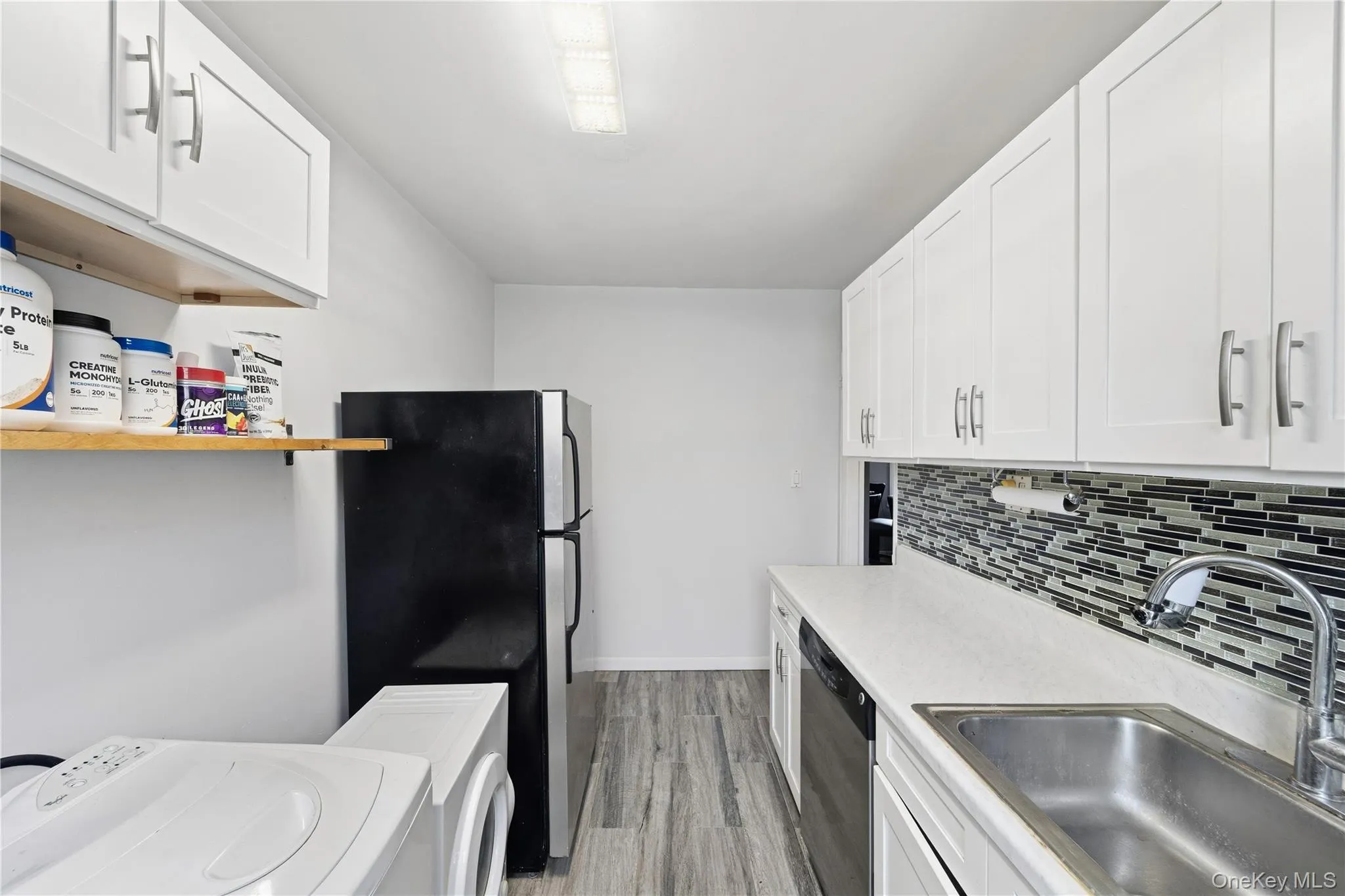 Kitchen with white cabinets, washer / clothes dryer, appliances with stainless steel finishes, and light wood-style flooring Kitchen with white cabinets, washer / clothes dryer, appliances with stainless steel finishes, and light wood-style flooring