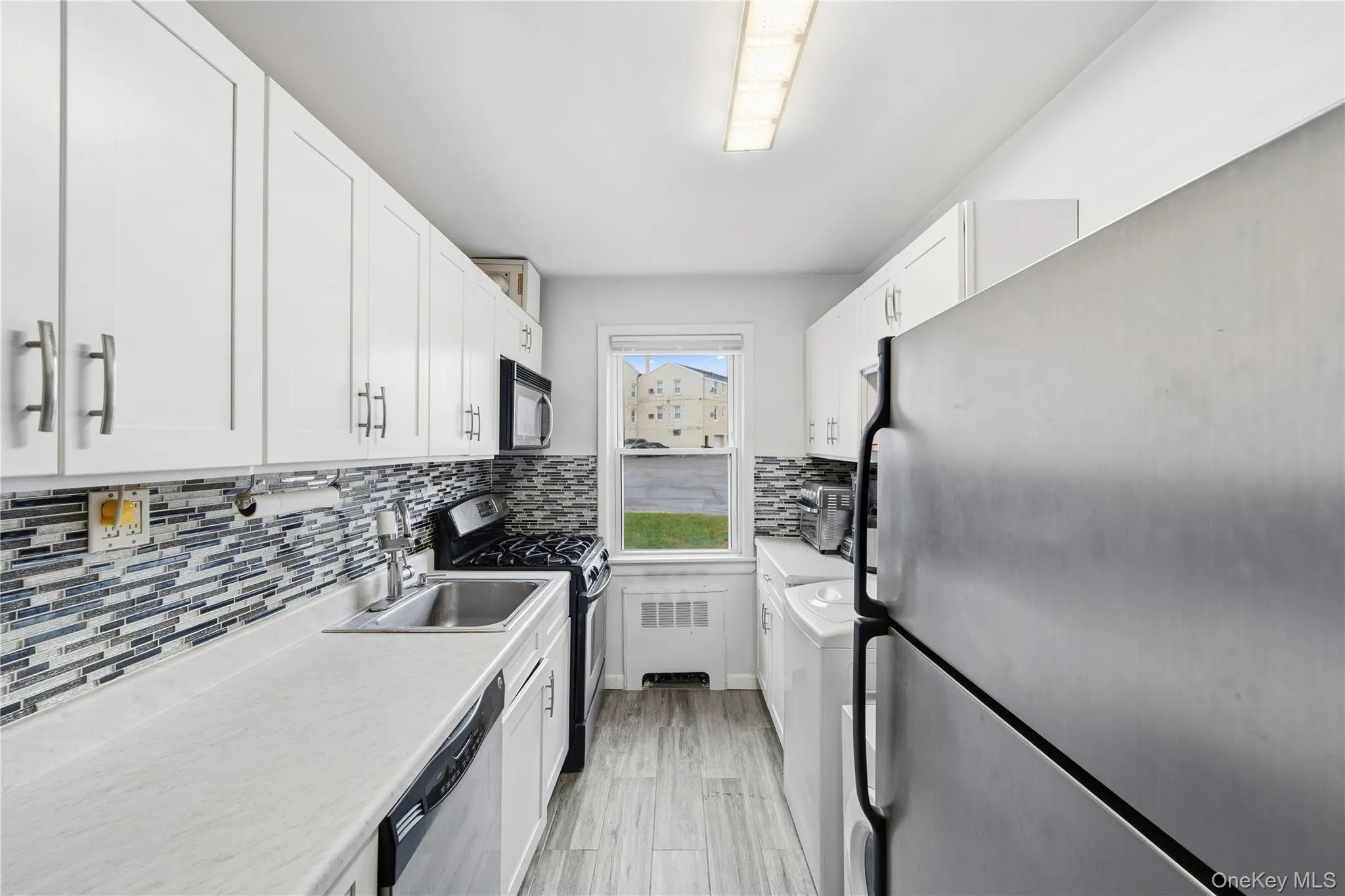 Kitchen with stainless steel appliances, white cabinetry, light countertops, backsplash, and washer / dryer Kitchen with stainless steel appliances, white cabinetry, light countertops, backsplash, and washer / dryer