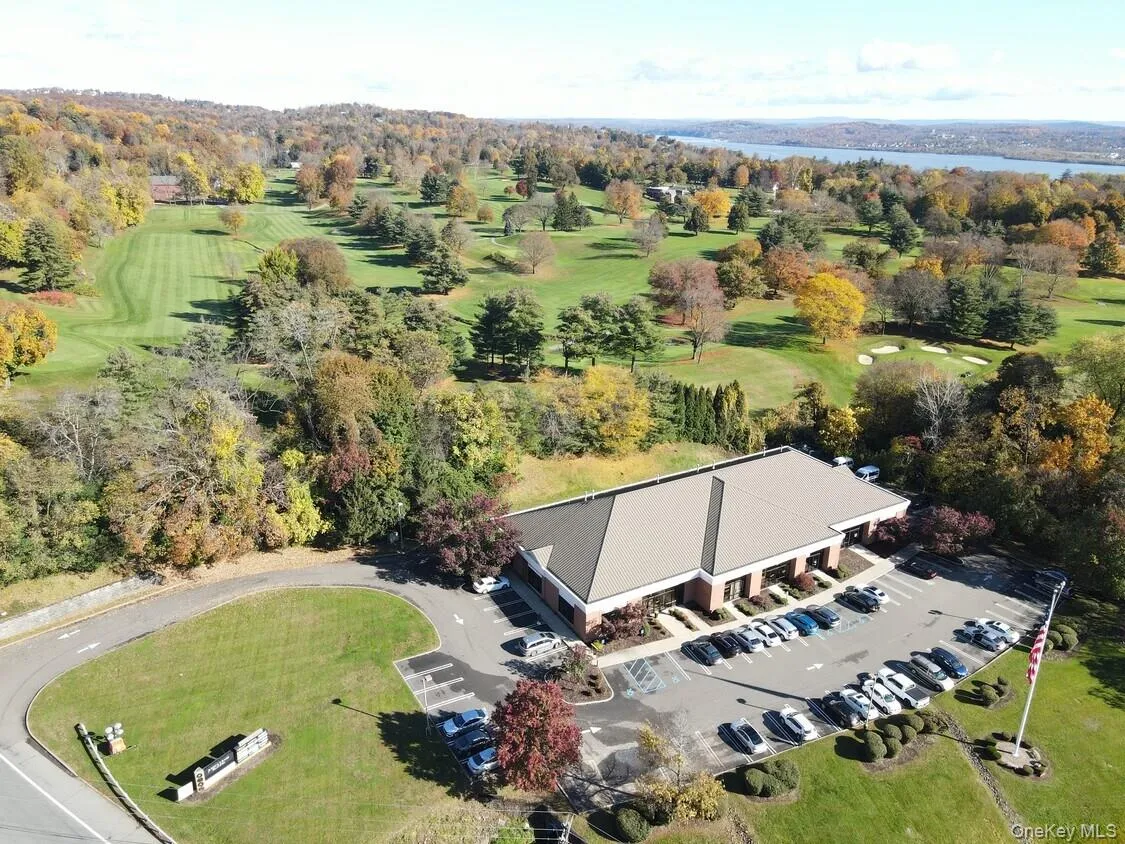 Commercial building with expansive parking lot, surrounded by mature trees, and bordered by a manicured golf course Commercial building with expansive parking lot, surrounded by mature trees, and bordered by a manicured golf course