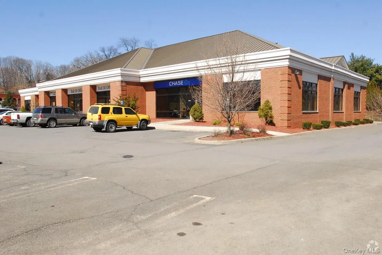 Brick building with multiple storefronts, featuring large storefront windows and a paved parking area Brick building with multiple storefronts, featuring large storefront windows and a paved parking area