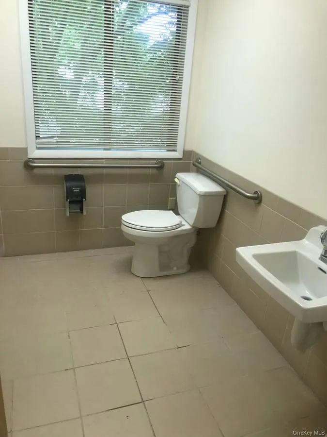 Bathroom with tile walls, healthy amount of natural light, a wainscoted wall, and light tile patterned floors Bathroom with tile walls, healthy amount of natural light, a wainscoted wall, and light tile patterned floors