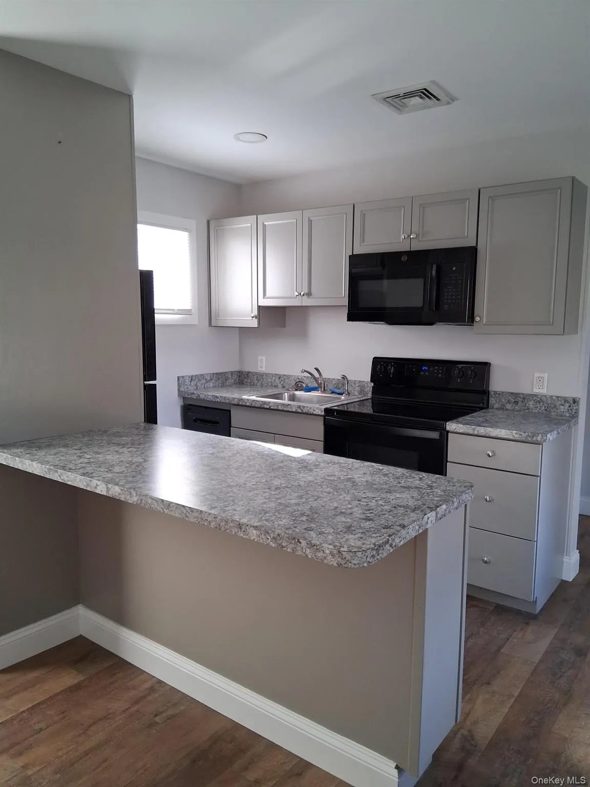 Kitchen with black appliances, gray cabinets, a peninsula, dark wood-type flooring, and light countertops Kitchen with black appliances, gray cabinets, a peninsula, dark wood-type flooring, and light countertops