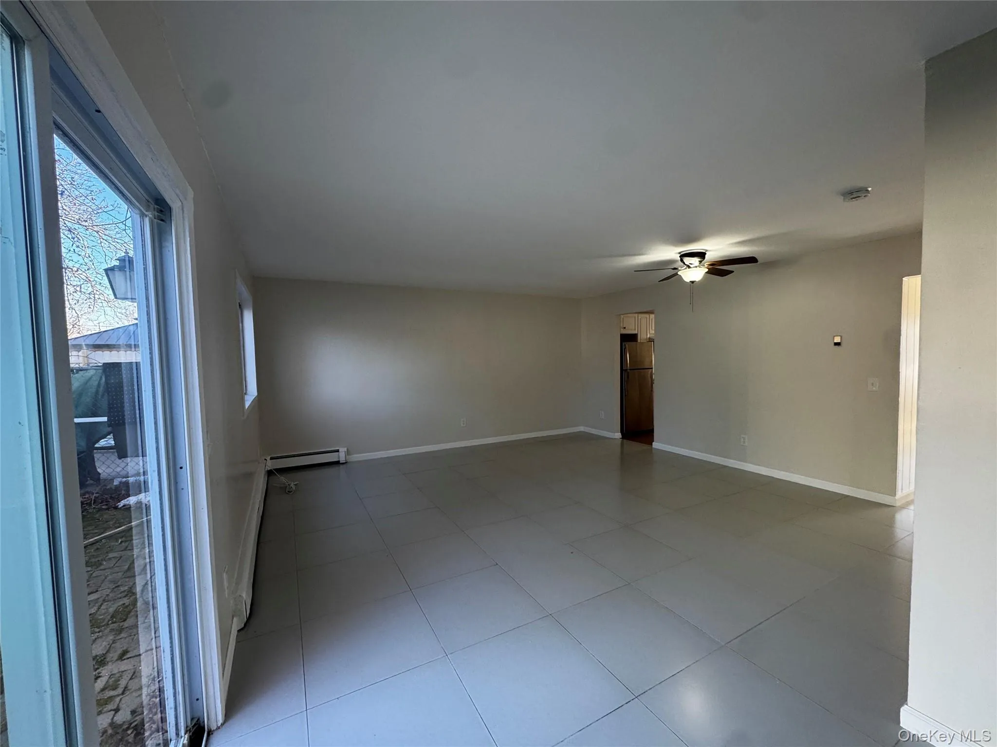 Dining/Living room combo with ceiling fan, light tile patterned floors, and a baseboard heating. Sliding door to rear yard and patio. Dining/Living room combo with ceiling fan, light tile patterned floors, and a baseboard heating. Sliding door to rear yard and patio.