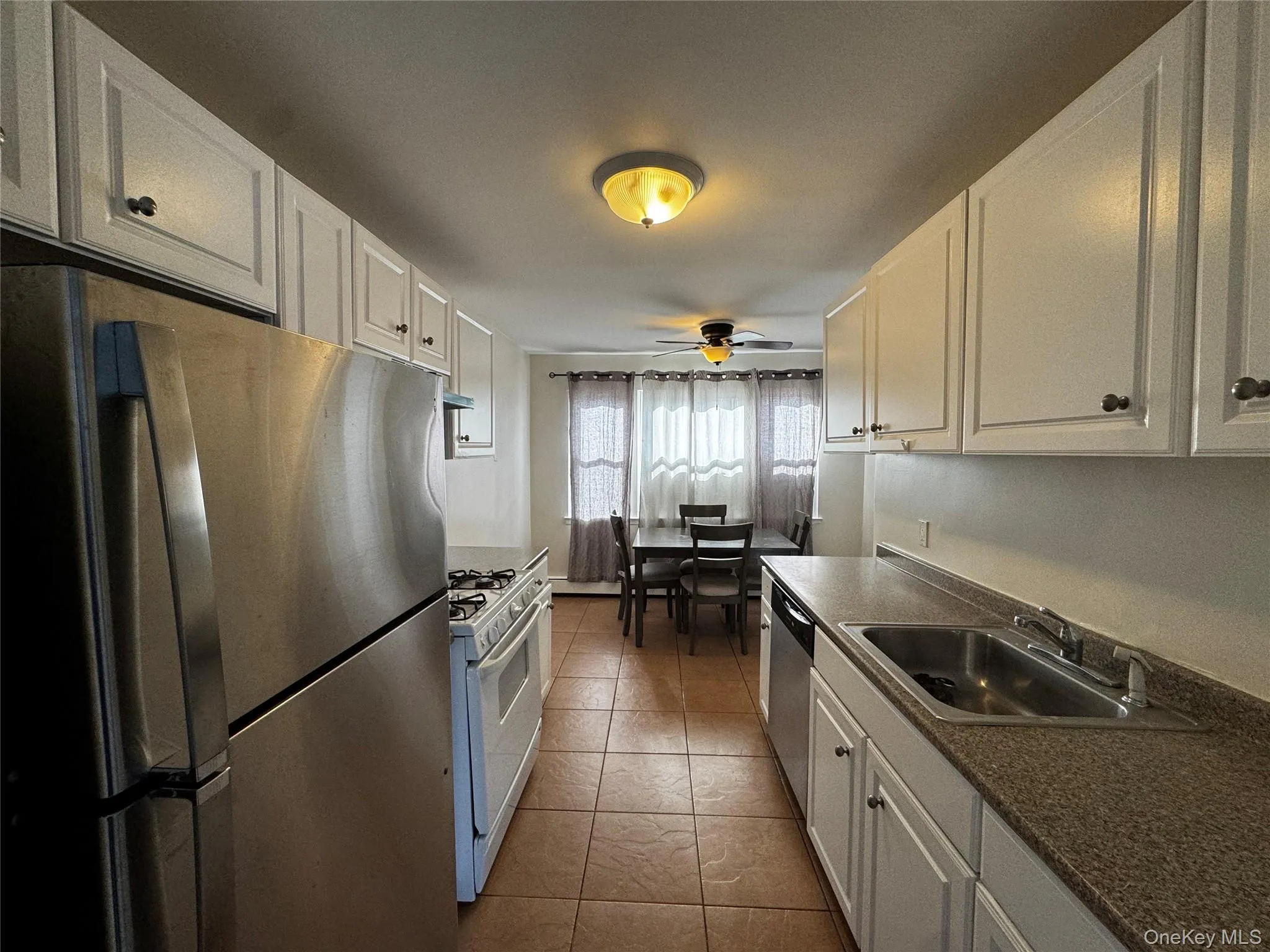 Kitchen featuring appliances with stainless steel finishes, white cabinets, dark countertops, a ceiling fan, and dark tile patterned flooring Kitchen featuring appliances with stainless steel finishes, white cabinets, dark countertops, a ceiling fan, and dark tile patterned flooring