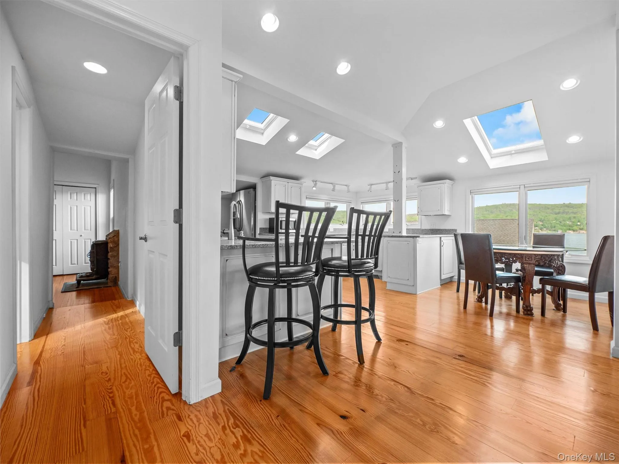 Kitchen featuring a peninsula, lofted ceiling, white cabinetry, light wood-type flooring, and a breakfast bar Kitchen featuring a peninsula, lofted ceiling, white cabinetry, light wood-type flooring, and a breakfast bar