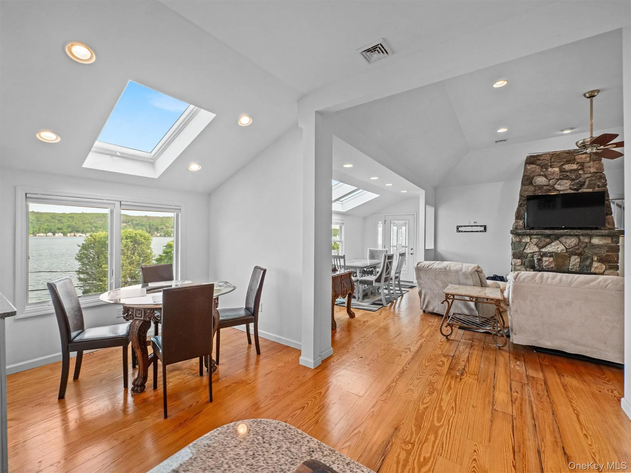 Dining room featuring vaulted ceiling, a fireplace, light wood-type flooring, a skylight, and recessed lighting Dining room featuring vaulted ceiling, a fireplace, light wood-type flooring, a skylight, and recessed lighting