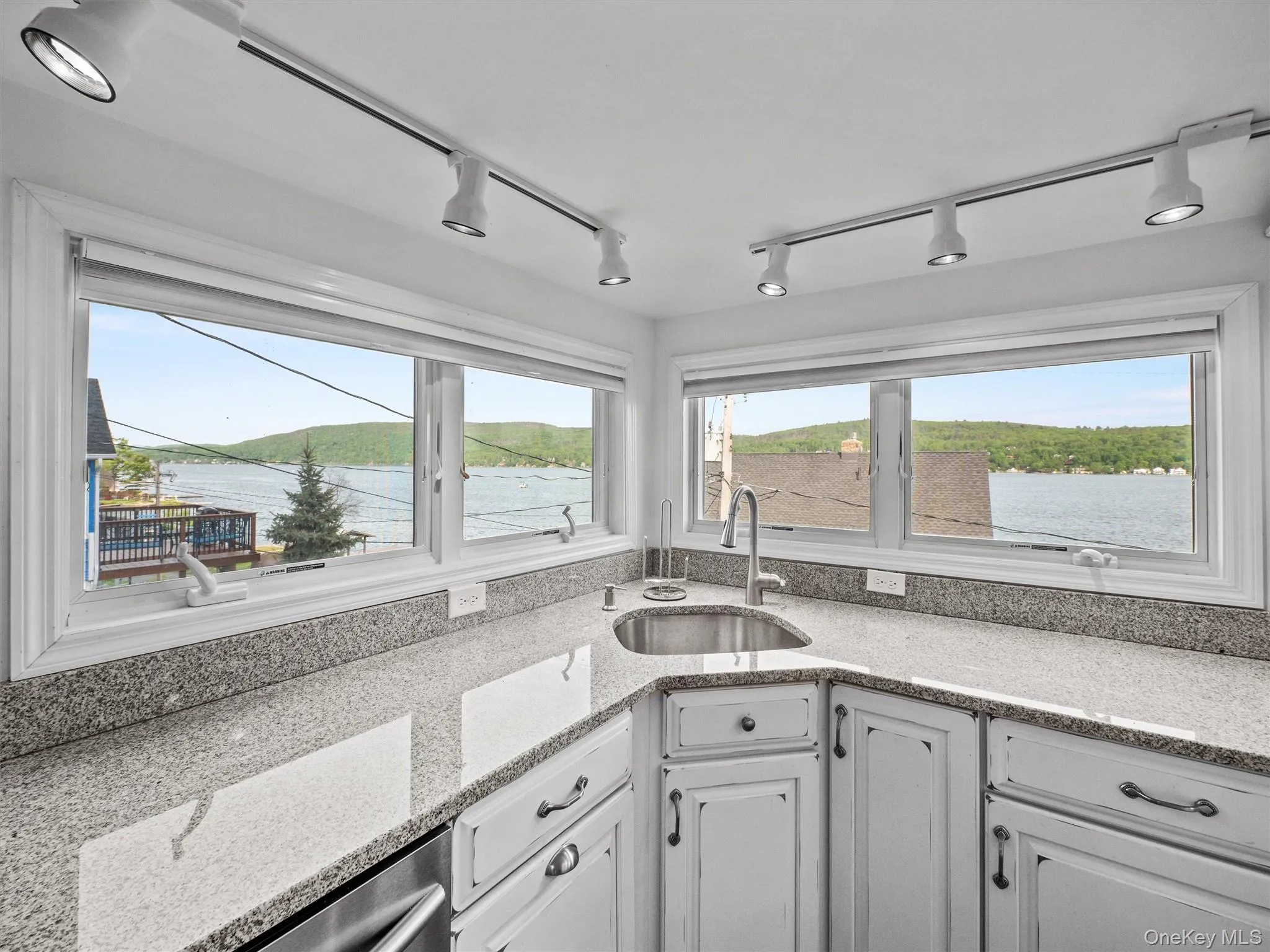 Kitchen with rail lighting, light stone countertops, healthy amount of natural light, and white cabinetry Kitchen with rail lighting, light stone countertops, healthy amount of natural light, and white cabinetry