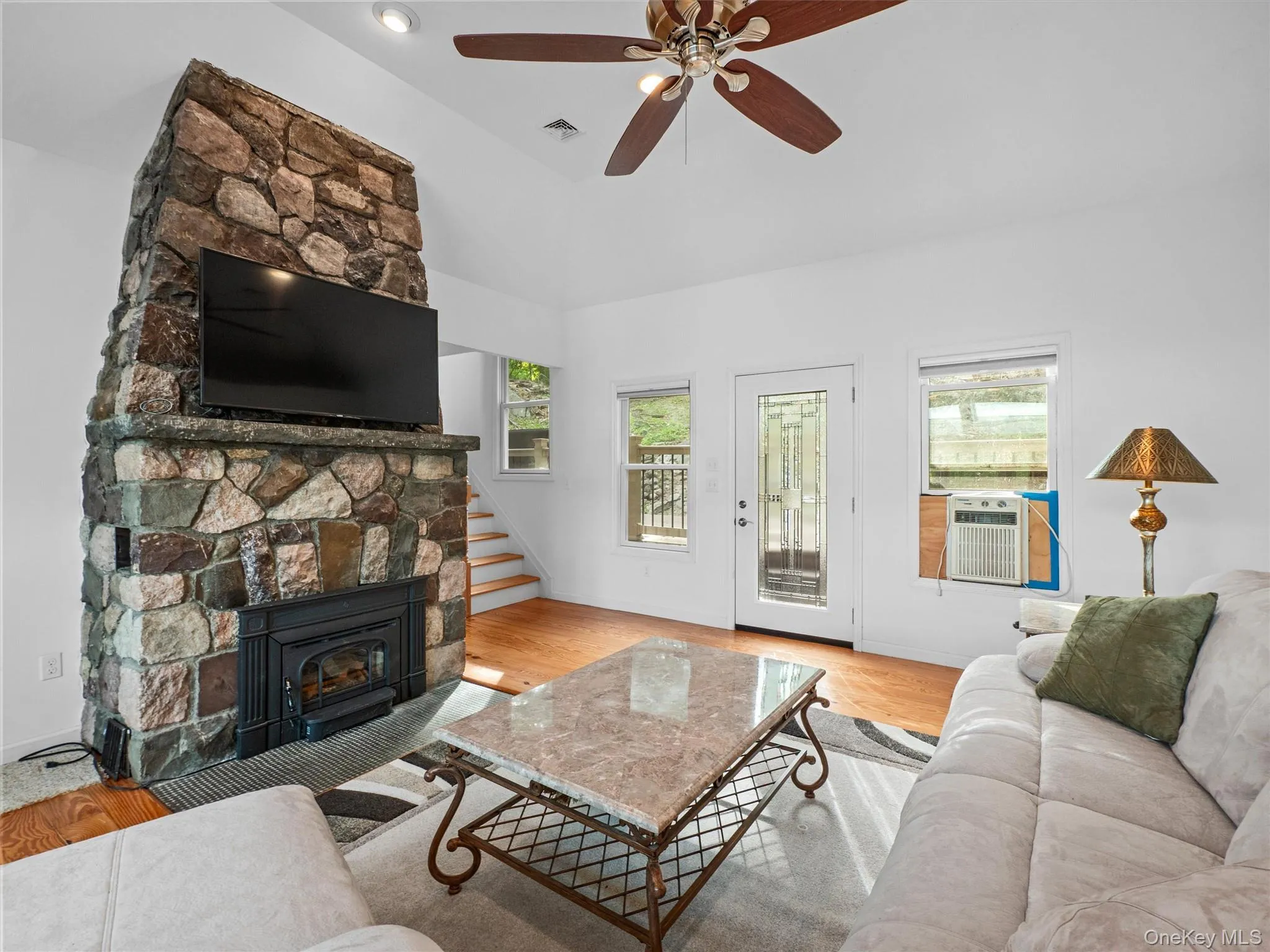 Living area with stairway, wood finished floors, a stone fireplace, ceiling fan, and lofted ceiling Living area with stairway, wood finished floors, a stone fireplace, ceiling fan, and lofted ceiling