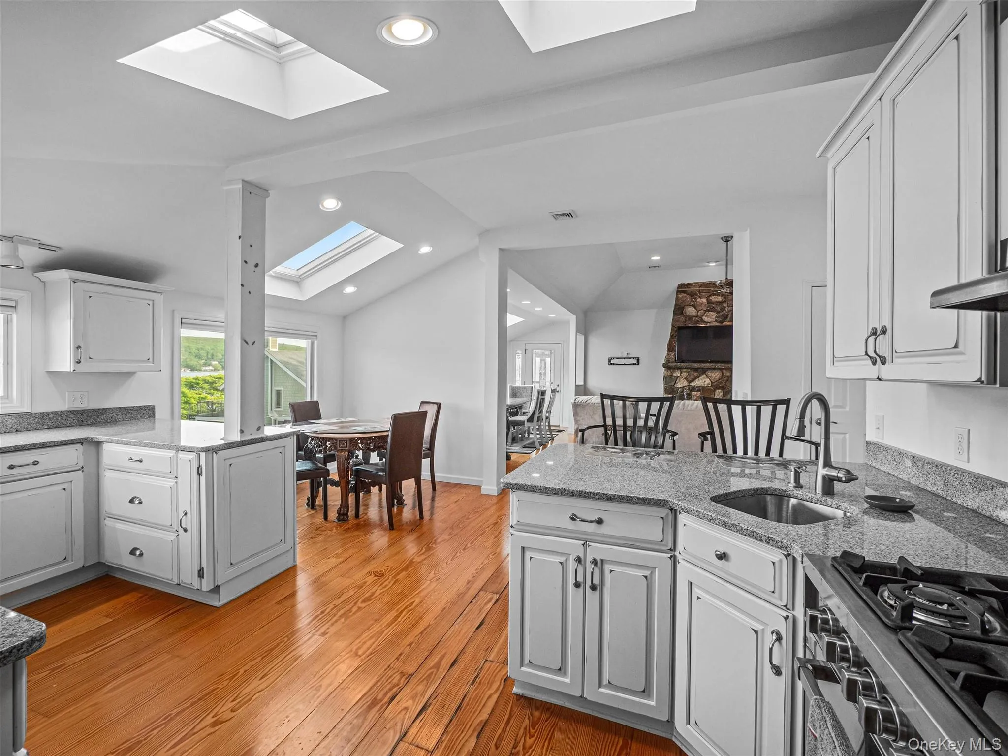 Kitchen with a peninsula, vaulted ceiling, range with gas cooktop, light stone counters, and white cabinets Kitchen with a peninsula, vaulted ceiling, range with gas cooktop, light stone counters, and white cabinets