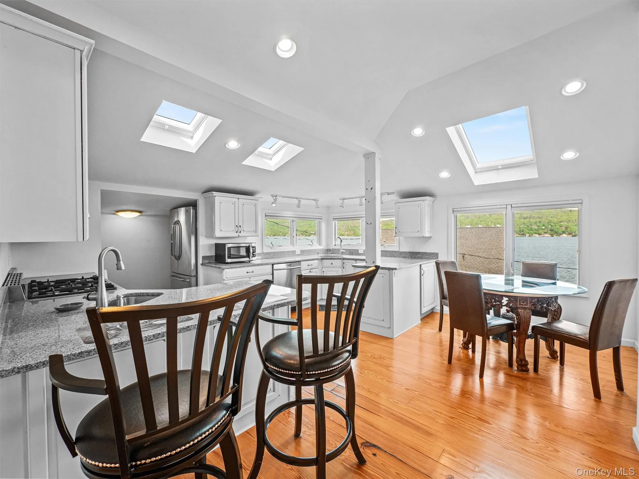 Kitchen featuring vaulted ceiling, a breakfast bar area, white cabinetry, a peninsula, and light wood-style flooring Kitchen featuring vaulted ceiling, a breakfast bar area, white cabinetry, a peninsula, and light wood-style flooring