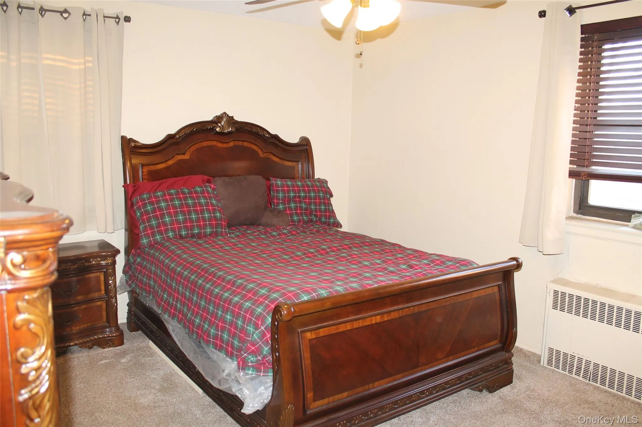 Carpeted bedroom with radiator heating unit, a ceiling fan, and multiple windows Carpeted bedroom with radiator heating unit, a ceiling fan, and multiple windows