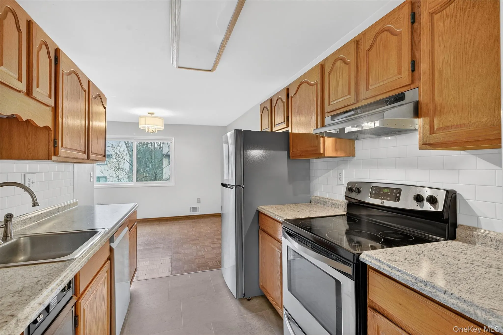 Kitchen with electric stove, decorative backsplash, under cabinet range hood, and white dishwasher Kitchen with electric stove, decorative backsplash, under cabinet range hood, and white dishwasher