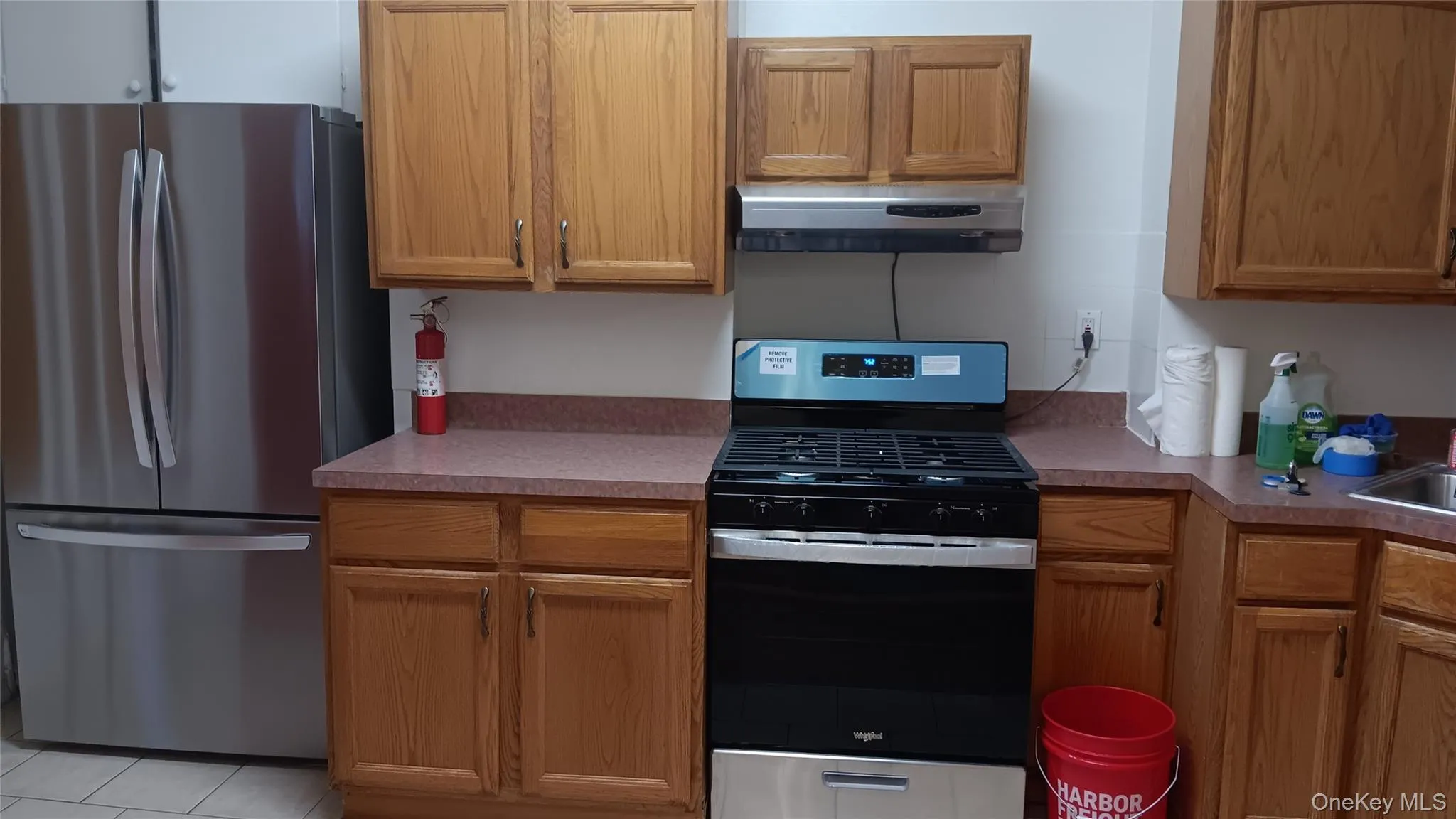 Kitchen featuring appliances with stainless steel finishes, brown cabinetry, extractor fan, and light tile patterned flooring Kitchen featuring appliances with stainless steel finishes, brown cabinetry, extractor fan, and light tile patterned flooring
