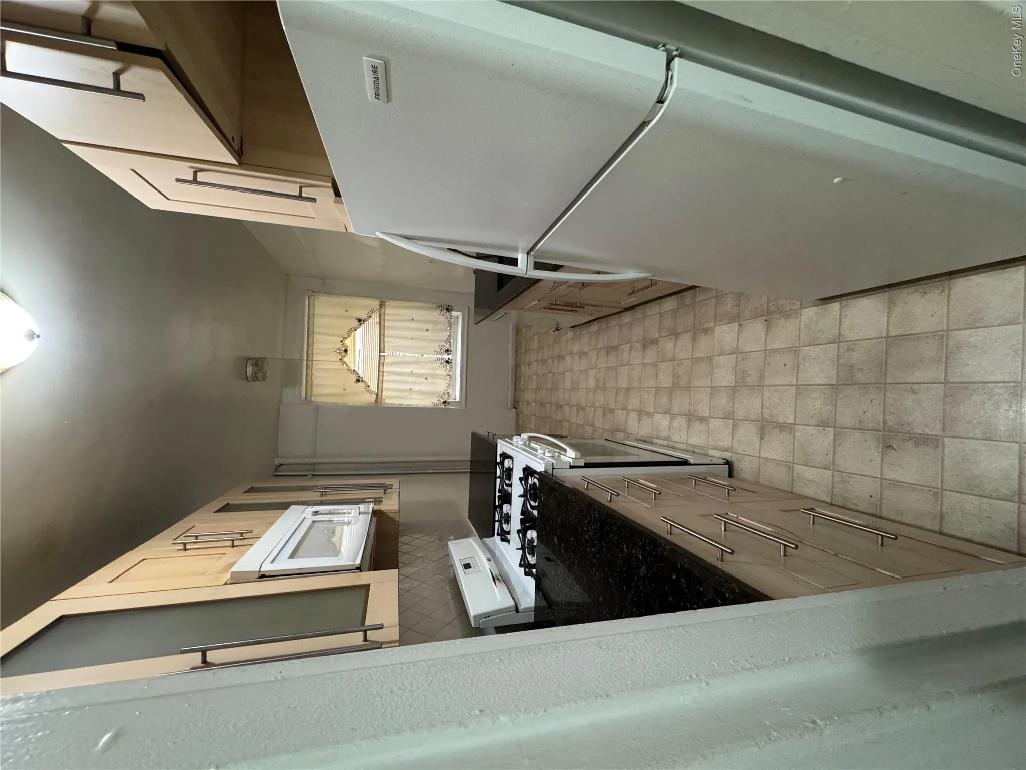 Kitchen featuring white appliances, light floors, light brown cabinetry, dark stone counters, and backsplash Kitchen featuring white appliances, light floors, light brown cabinetry, dark stone counters, and backsplash